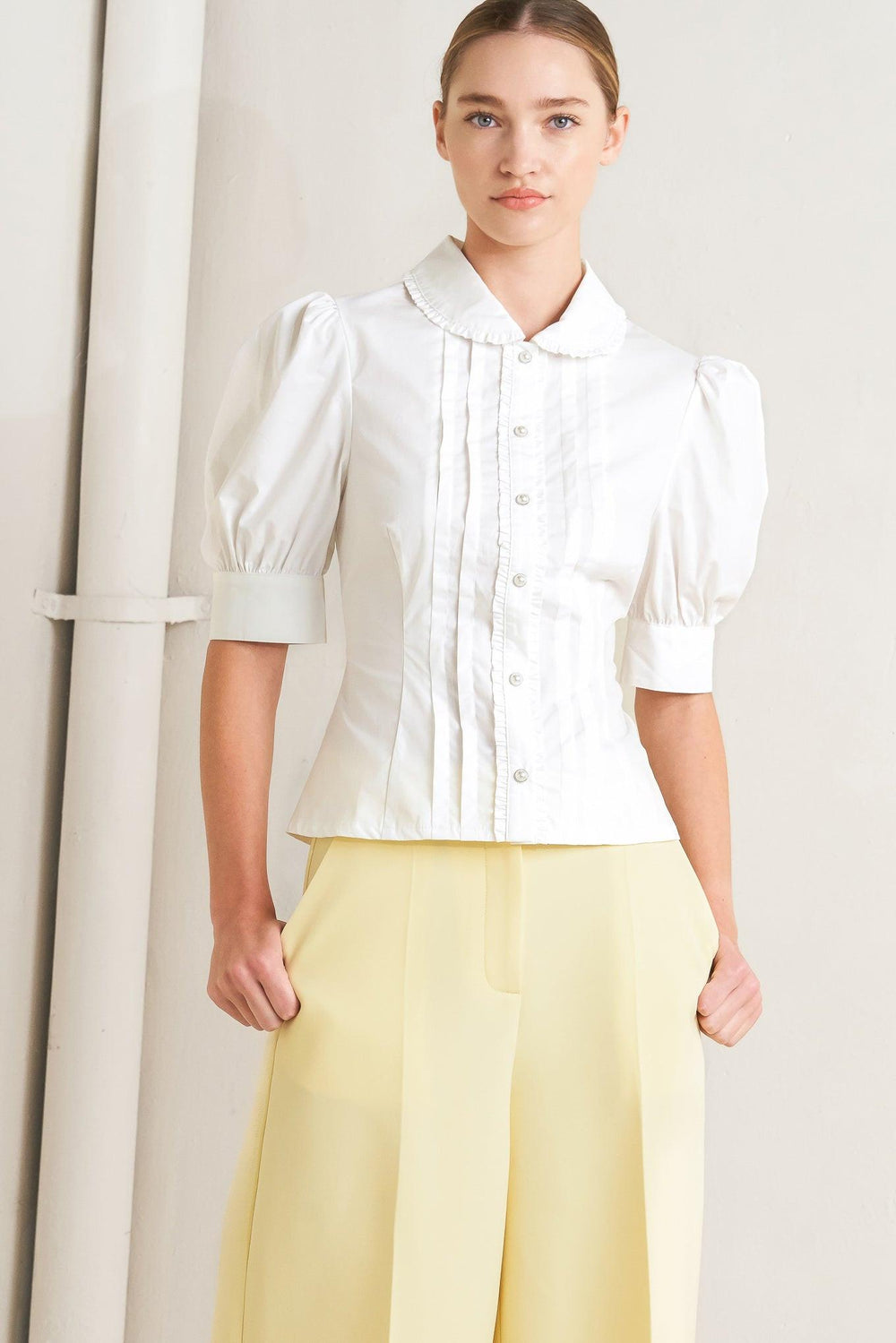 
A solid woven top featuring round collar with ruffle edge, short puff sleeve with cuff, front pintuck, ruffle edge placket with jewel button

Details:

Self : 100% Cotton

Size &amp; Fit

- Model is 5`8" And Wearing Size Small
- Measurements Taken From Size Small
- Approx. Length: 22" Flying Tomato