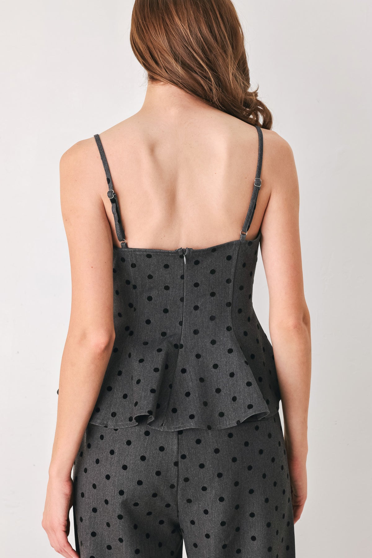 Woman wearing a spaghetti strap charcoal grey top with black polka dots and a peplum waist | FREEMARKET