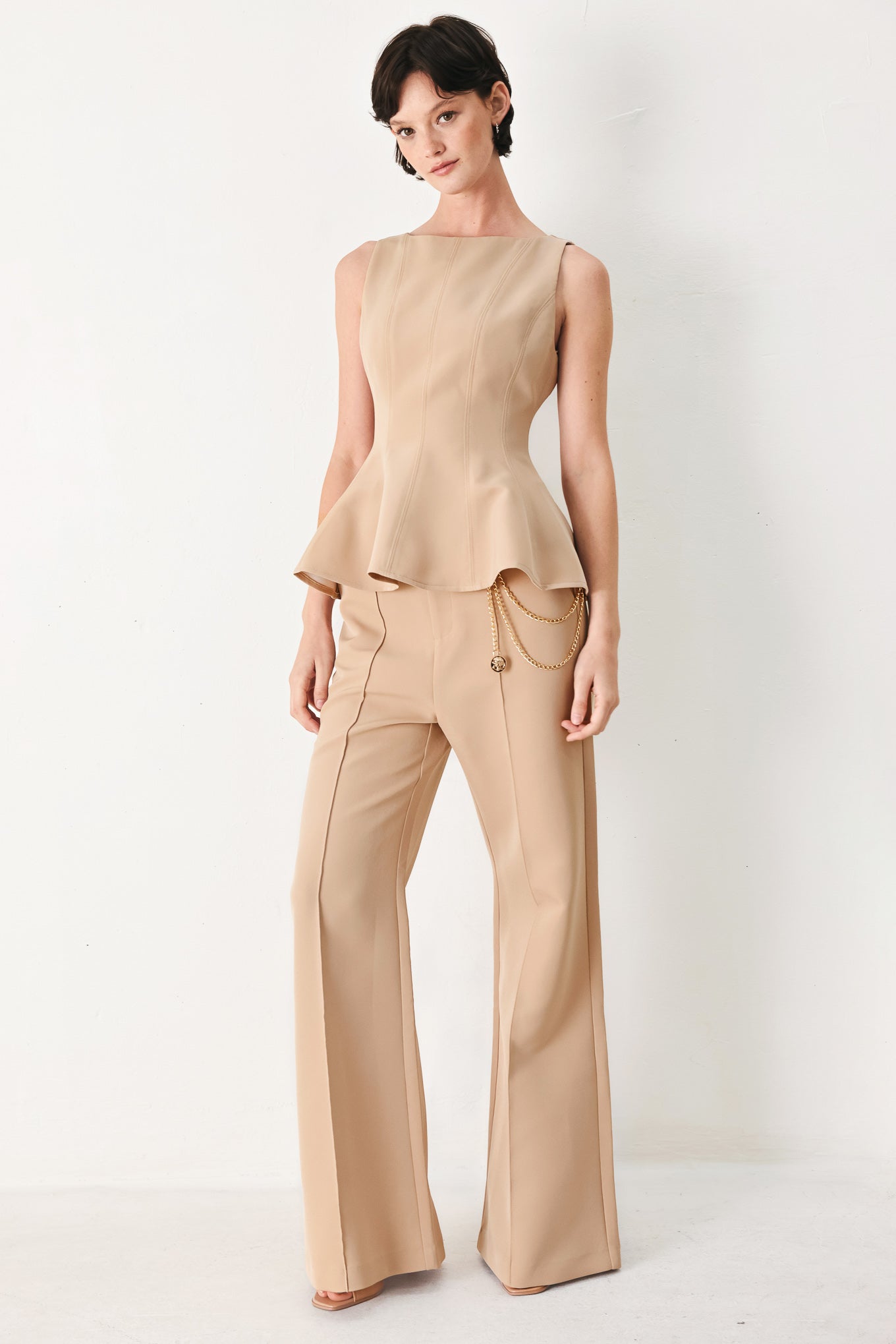 Woman wearing a camel sleeveless top with boat neckline, peplum and back zipper closure | FREEMARKET