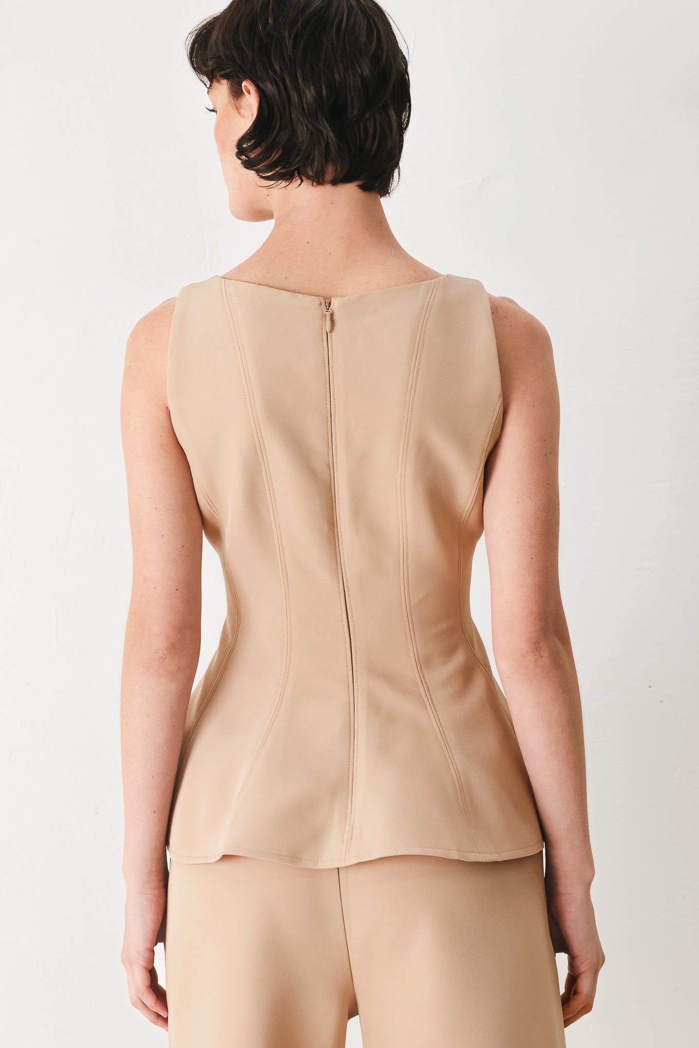 Woman wearing a camel sleeveless top with boat neckline, peplum and back zipper closure | FREEMARKET