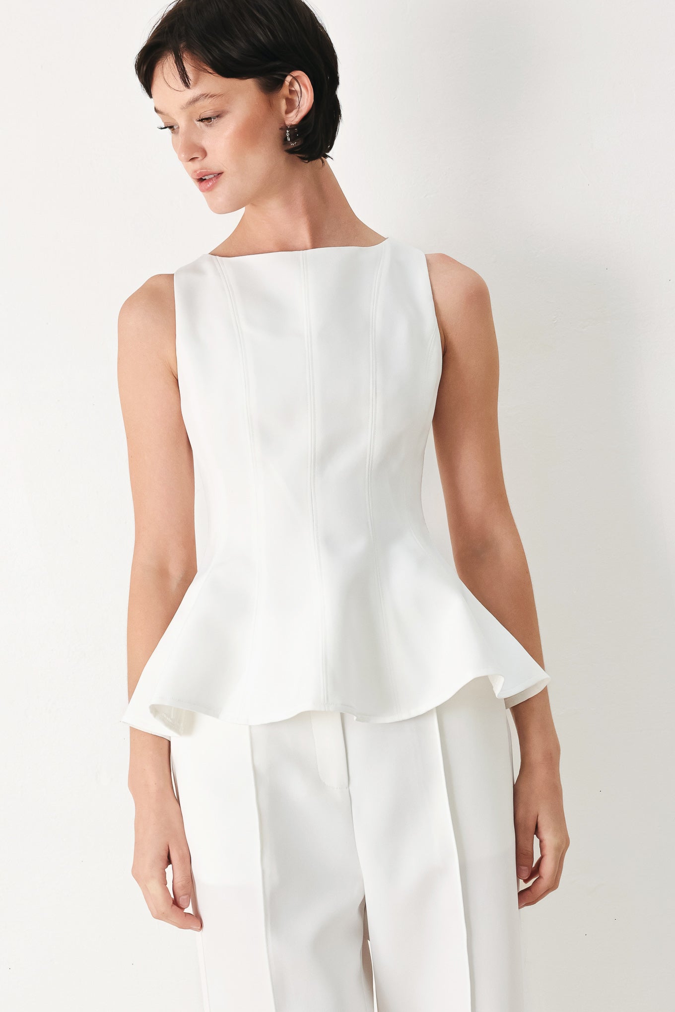 Woman wearing a white sleeveless top with boat neckline, peplum and back zipper closure | FREEMARKET