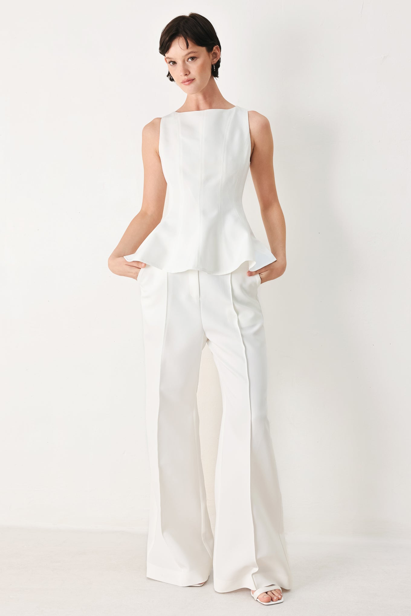 Woman wearing a white sleeveless top with boat neckline, peplum and back zipper closure | FREEMARKET