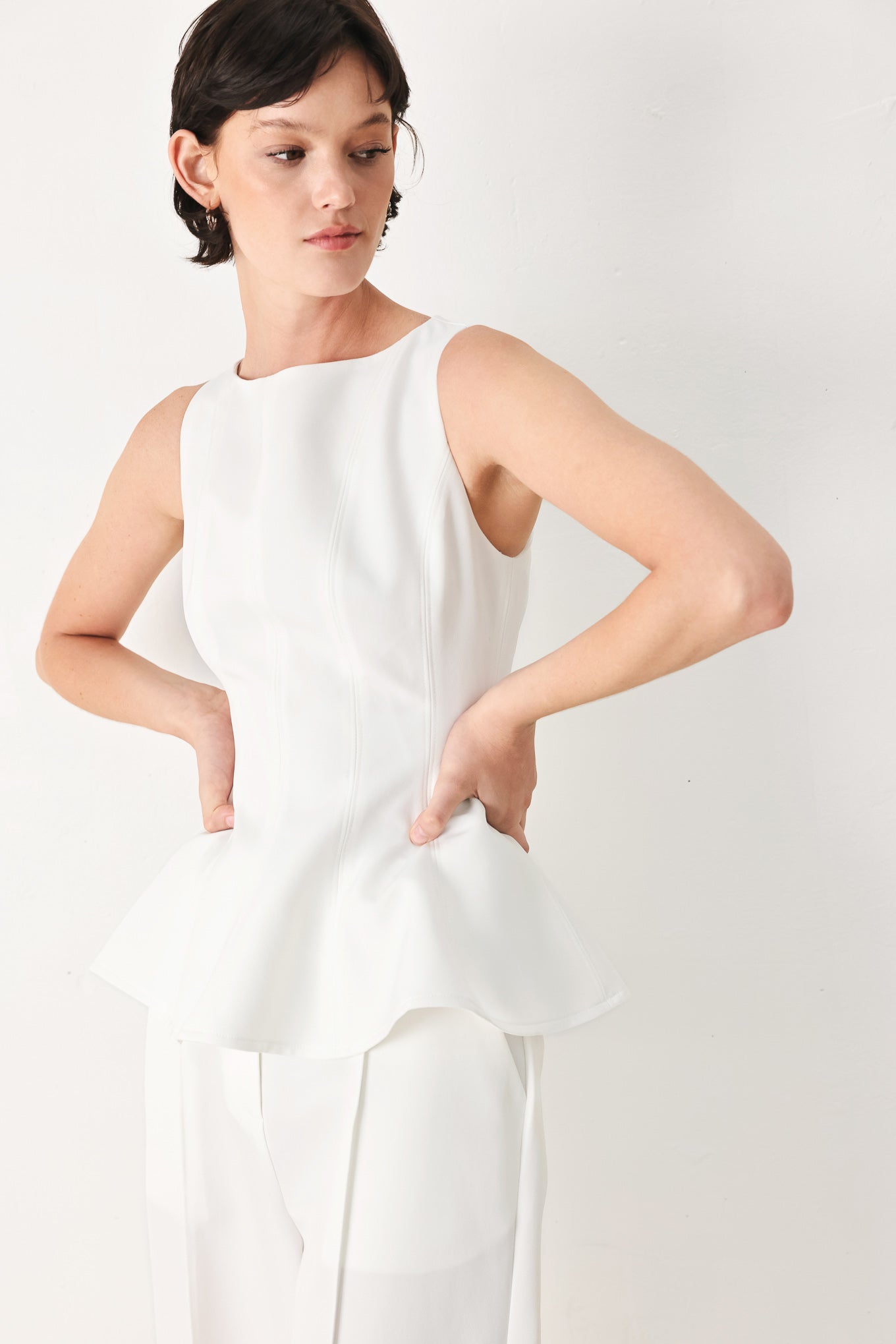 Woman wearing a white sleeveless top with boat neckline, peplum and back zipper closure | FREEMARKET