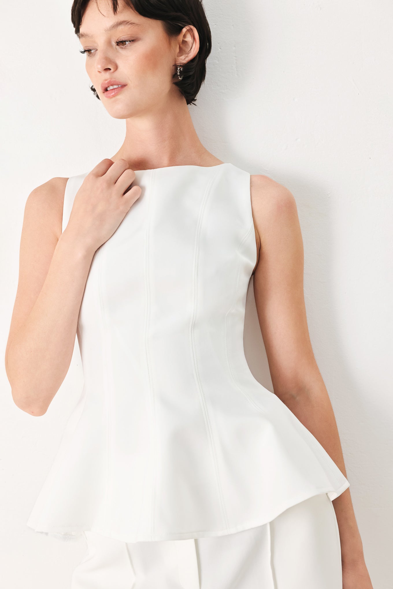 Woman wearing a white sleeveless top with boat neckline, peplum and back zipper closure | FREEMARKET