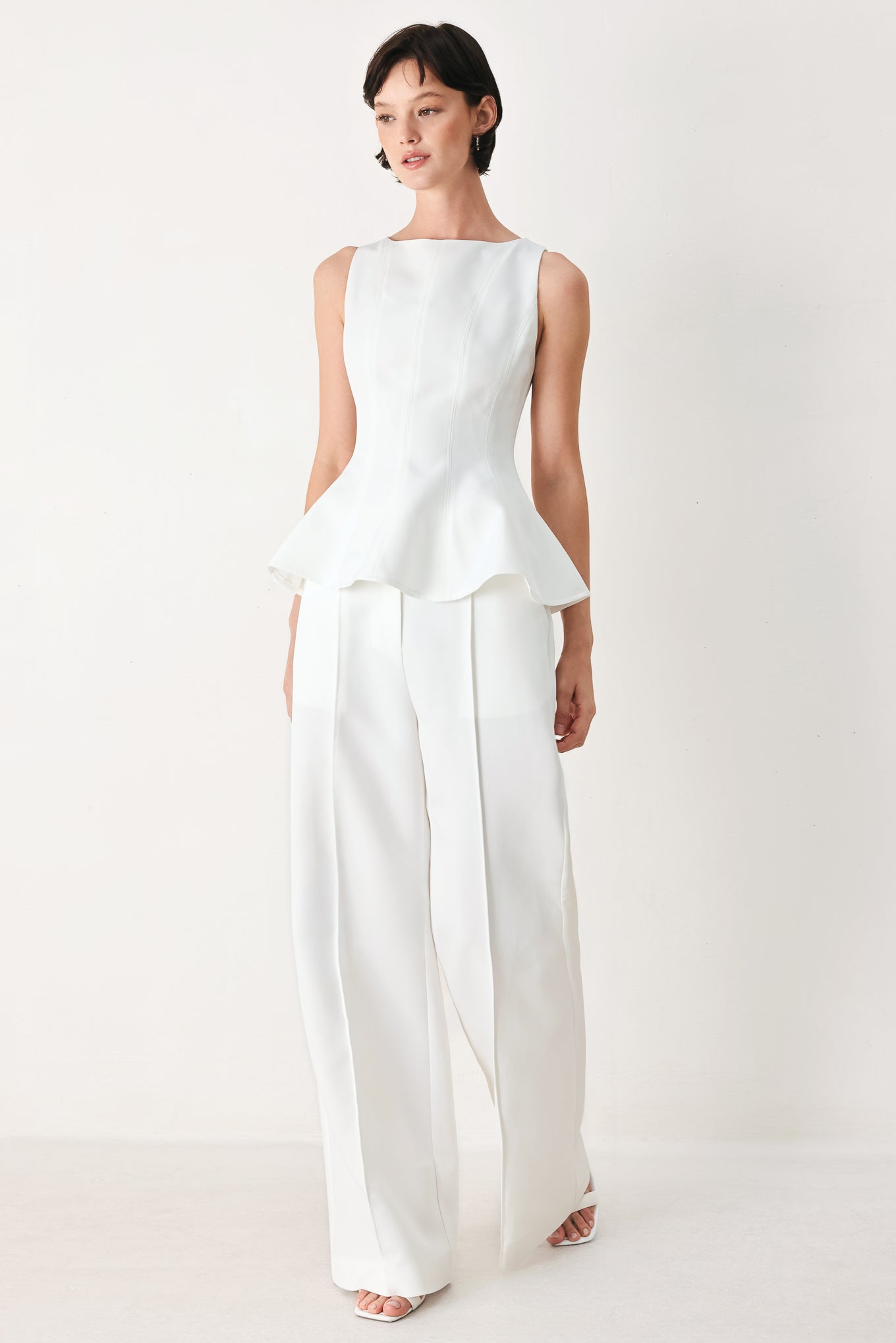 Woman wearing a white sleeveless top with boat neckline, peplum and back zipper closure | FREEMARKET