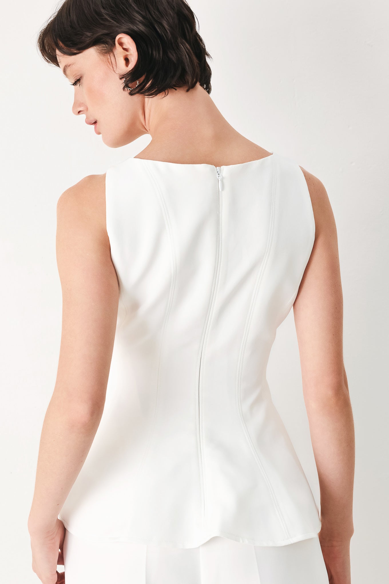 Woman wearing a white sleeveless top with boat neckline, peplum and back zipper closure | FREEMARKET