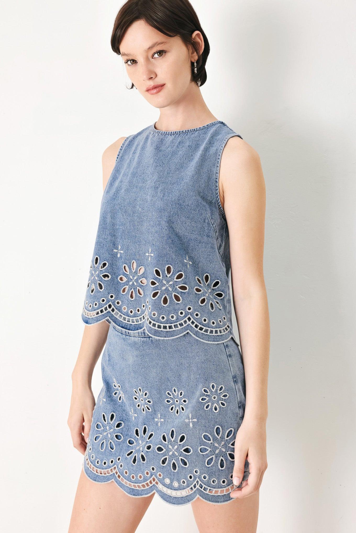 A washed denim top featuring round neckline, sleeveless, eyelet cut out and scallop hem with back tie closure