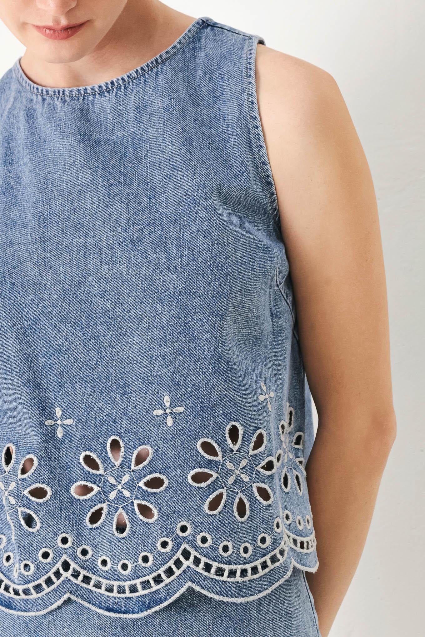 A washed denim top featuring round neckline, sleeveless, eyelet cut out and scallop hem with back tie closure