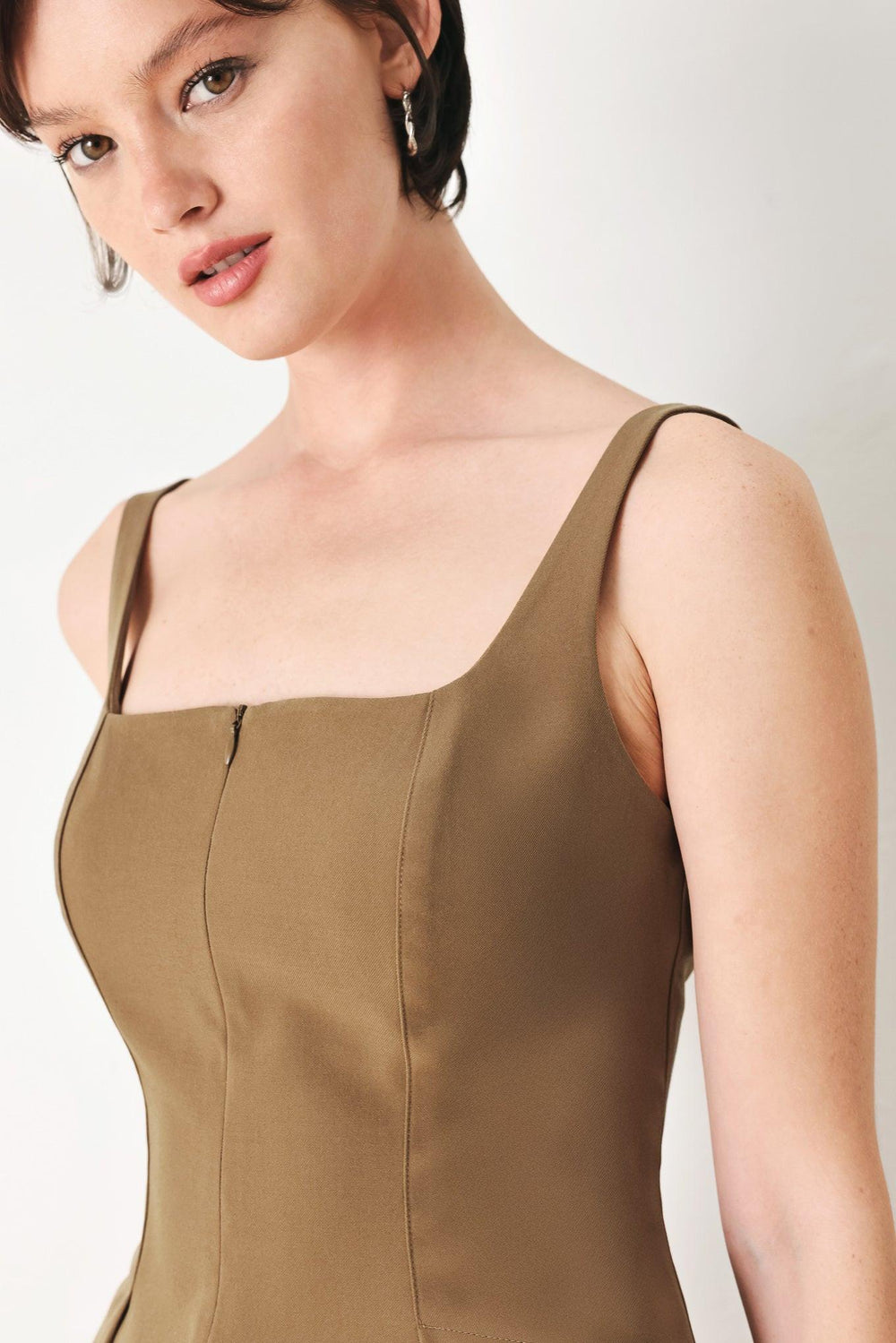 A solid woven top with square neckline, sleeveless, front zipper closure and peplum.