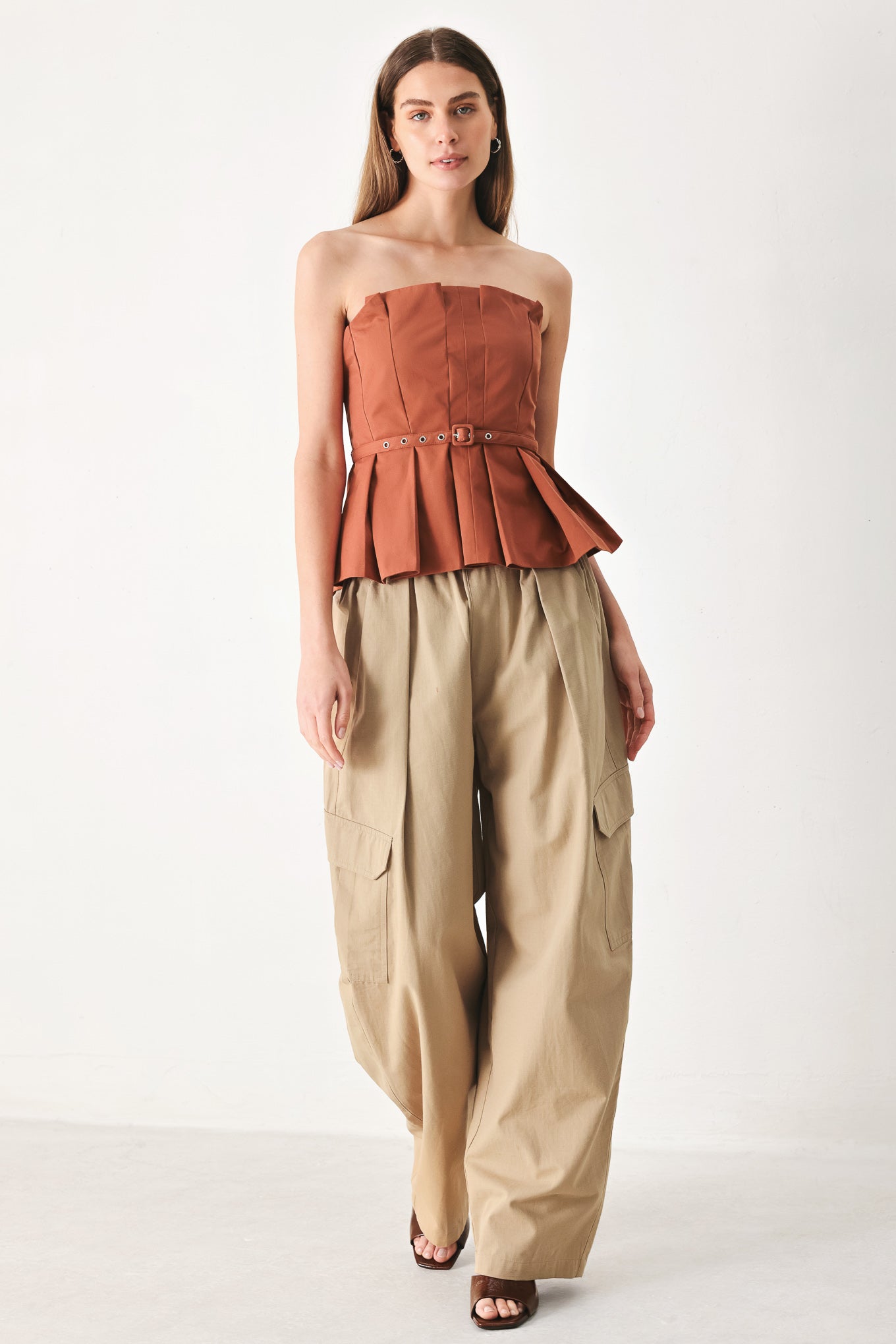 Woman wearing a rust-colored strapless top with a belt featuring knife pleats | Flying Tomato
