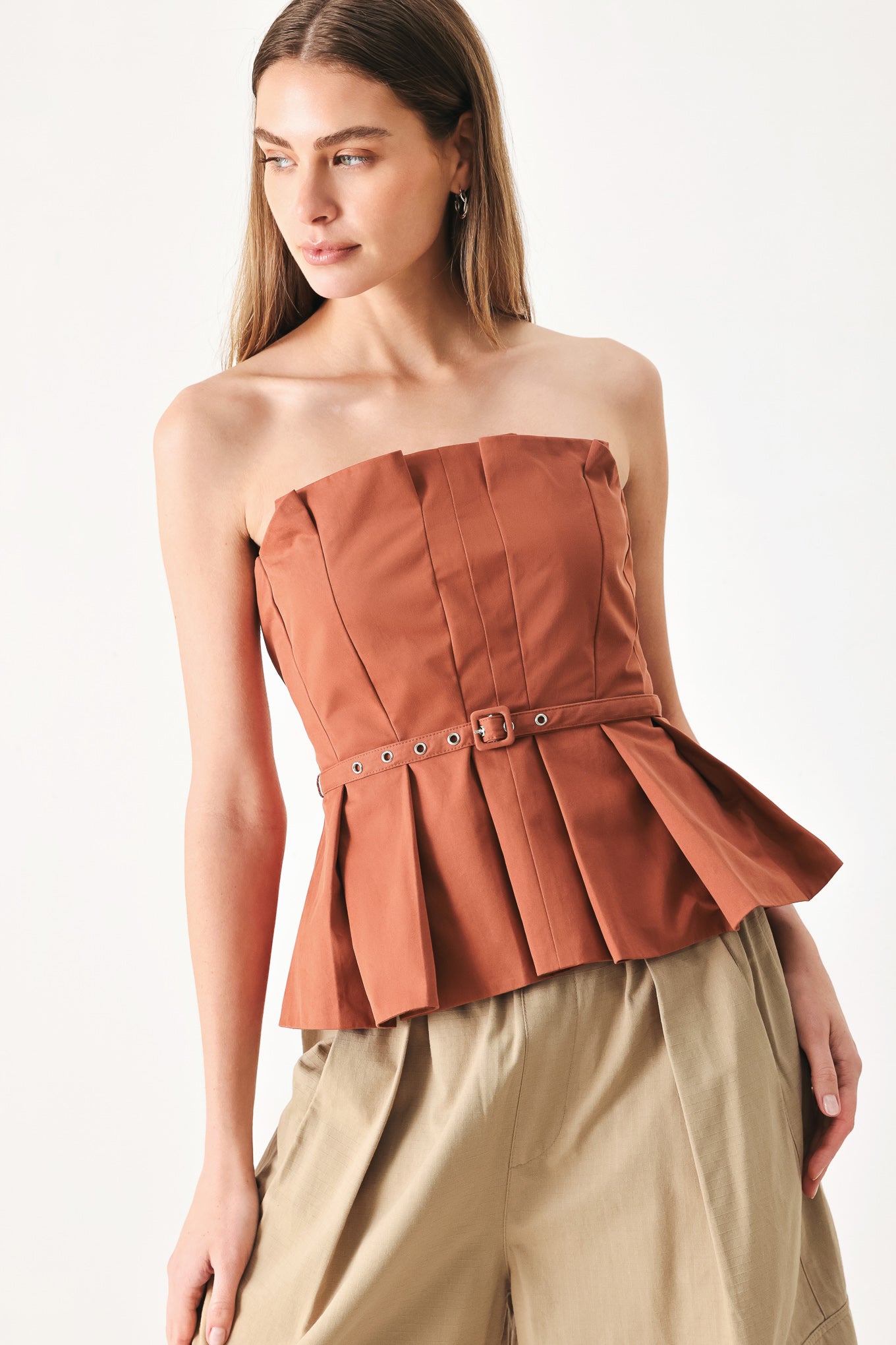 Woman wearing a rust-colored strapless top with a belt featuring knife pleats | Flying Tomato
