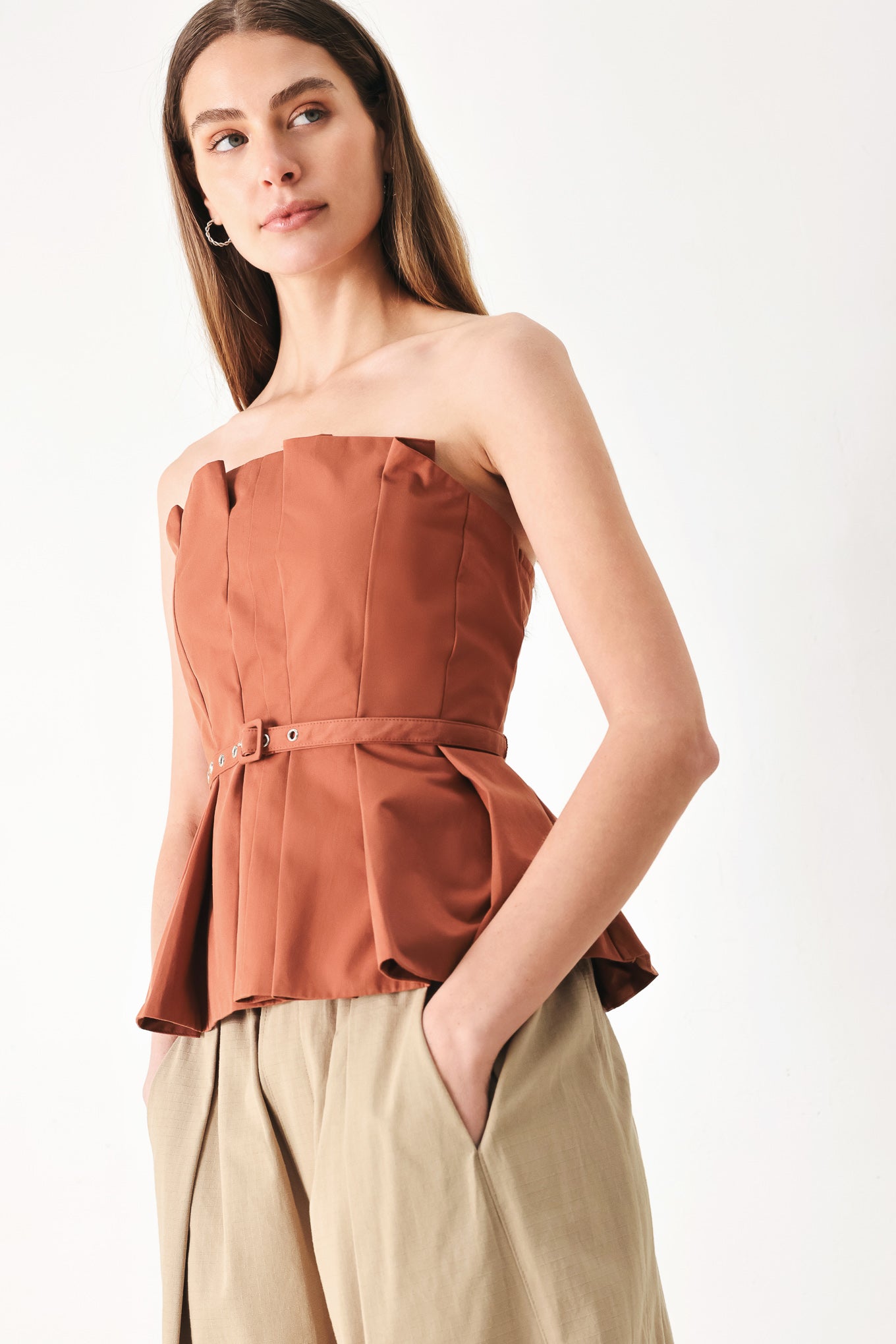 Woman wearing a rust-colored strapless top with a belt featuring knife pleats | Flying Tomato
