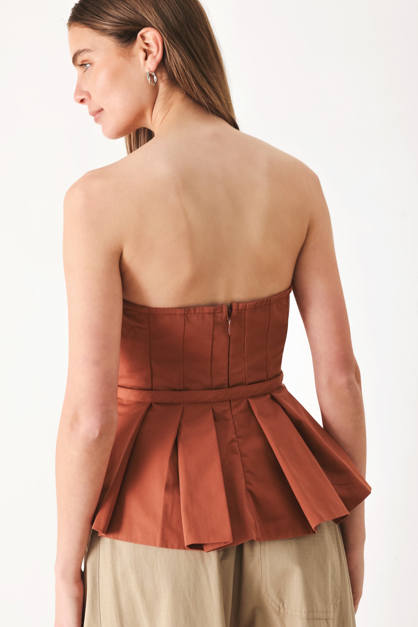 Woman wearing a rust-colored strapless top with a belt featuring knife pleats | Flying Tomato