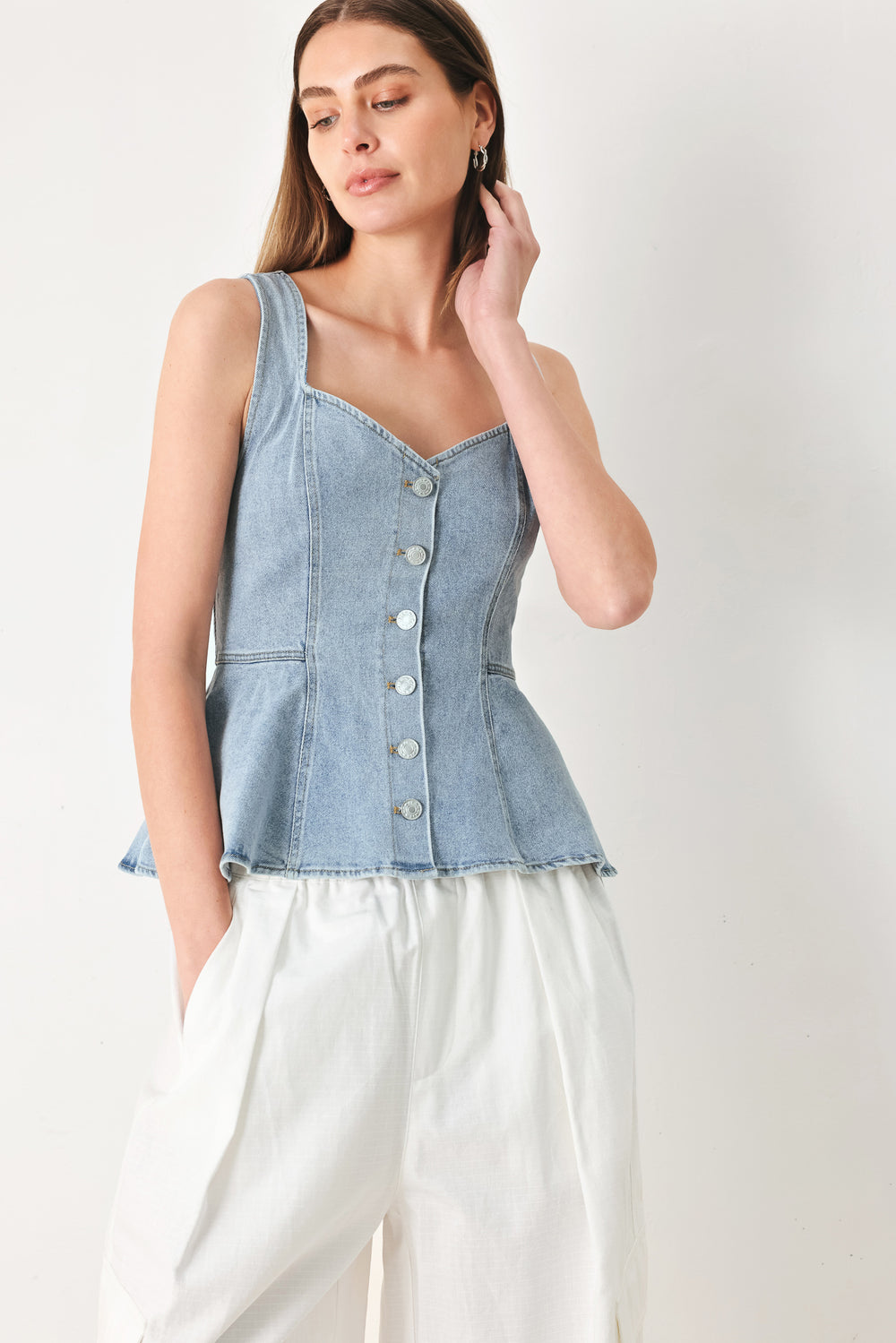Woman wearing a sleeveless denim peplum top featuring Queen Anne neckline, sleeveless, front button down | FREEMARKET | Flying Tomato