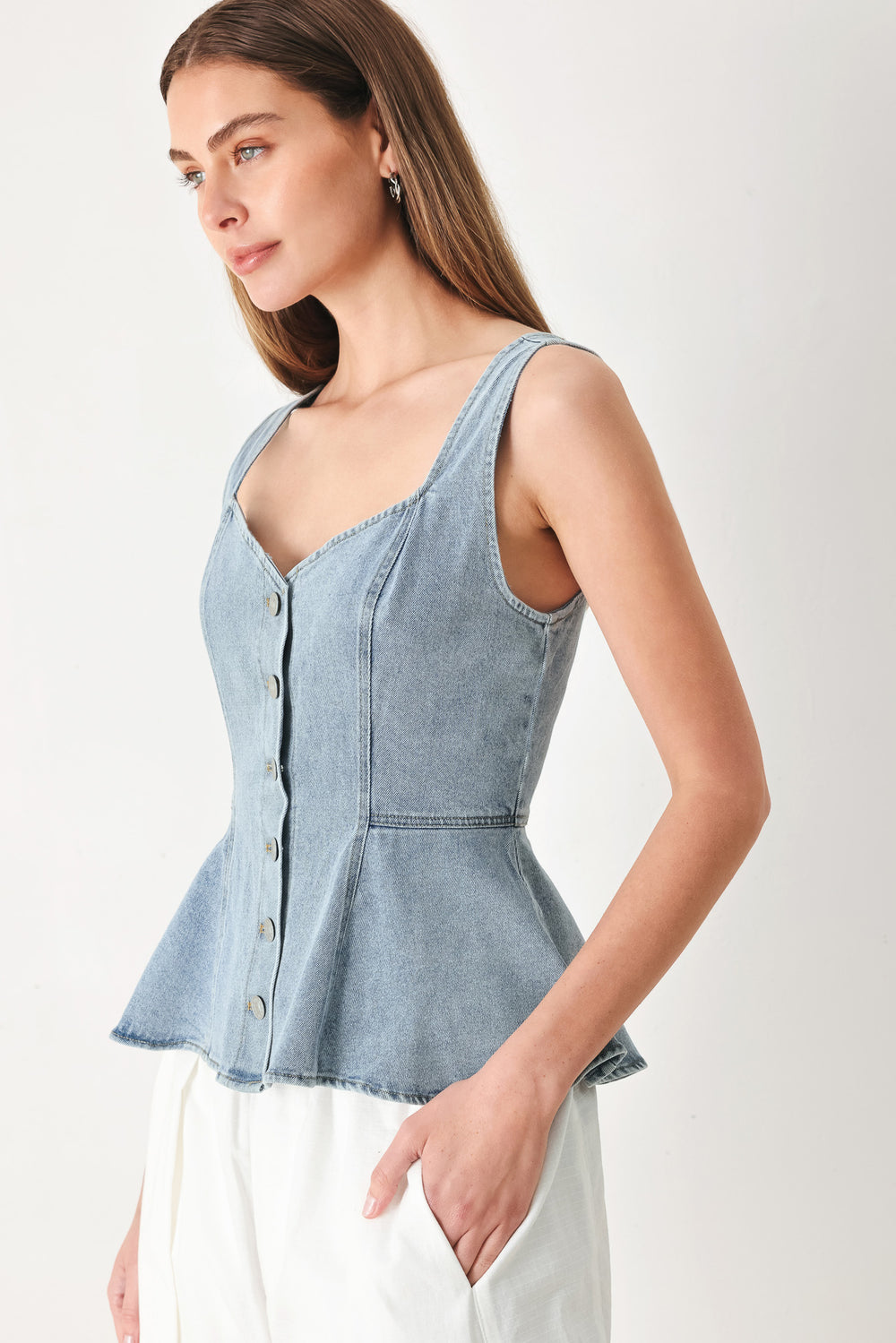 Woman wearing a sleeveless denim peplum top featuring Queen Anne neckline, sleeveless, front button down | FREEMARKET | Flying Tomato