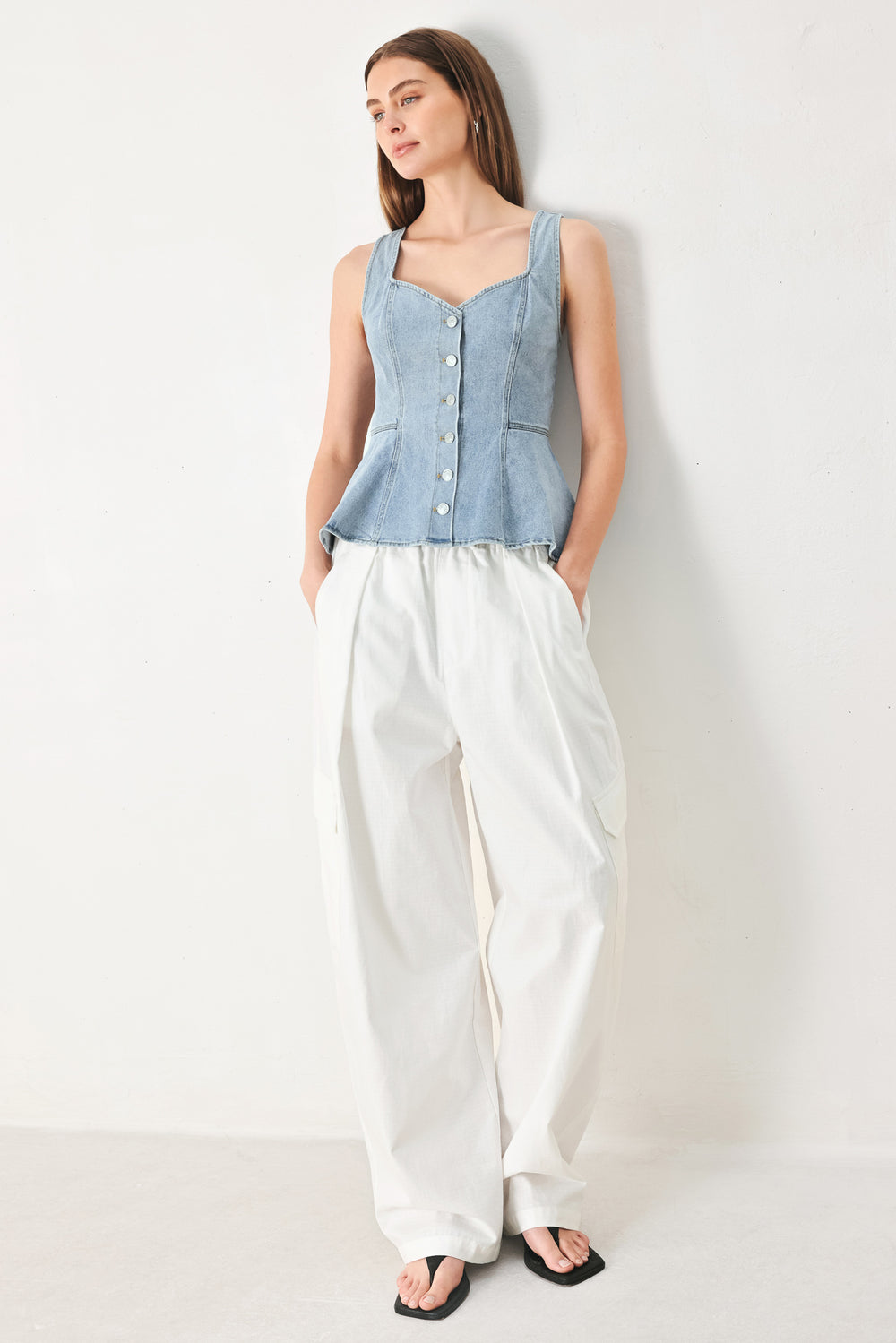 Woman wearing a sleeveless denim peplum top featuring Queen Anne neckline, sleeveless, front button down | FREEMARKET | Flying Tomato