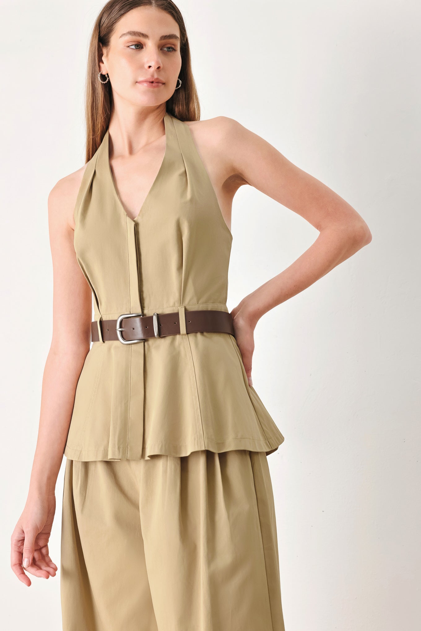 Woman wearing a beige halter peplum top with a brown belt with front closure | FREEMARKET | Flying Tomato