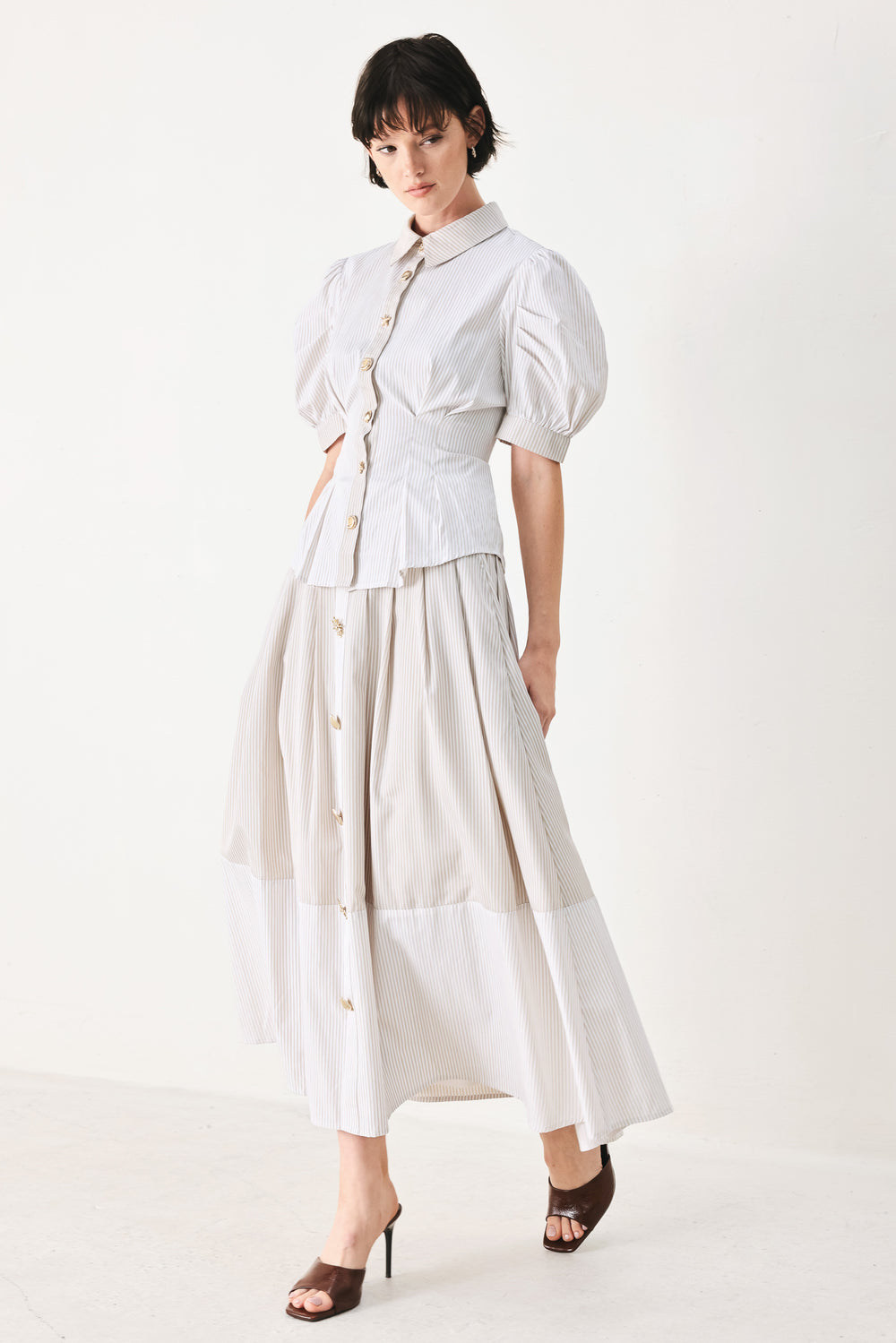 Woman wearing a taupe and white striped woven top featuring short puff sleeve, front button down, corset waist and peplum | FREEMARKET