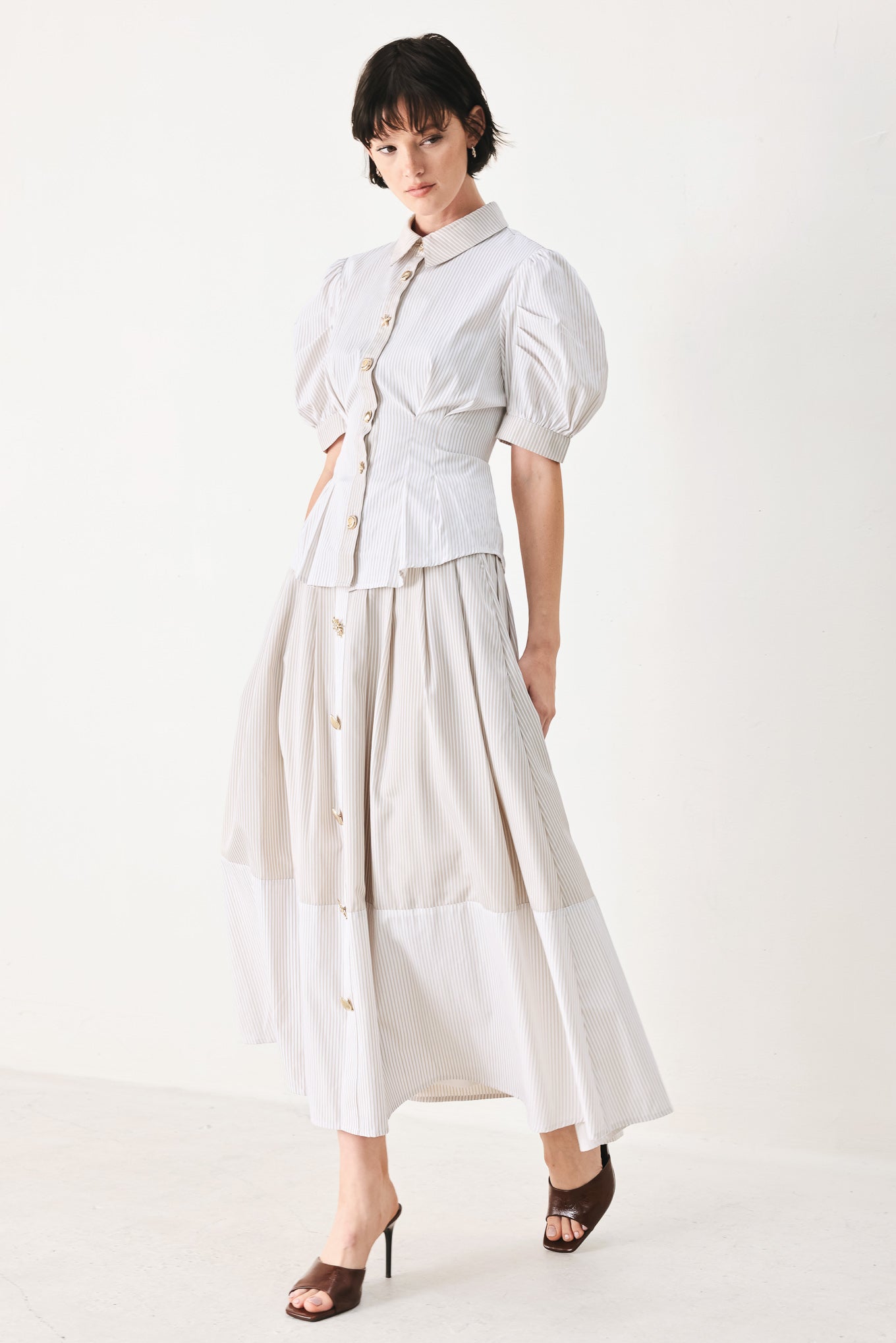 Woman wearing a taupe and white striped woven top featuring short puff sleeve, front button down, corset waist and peplum | FREEMARKET