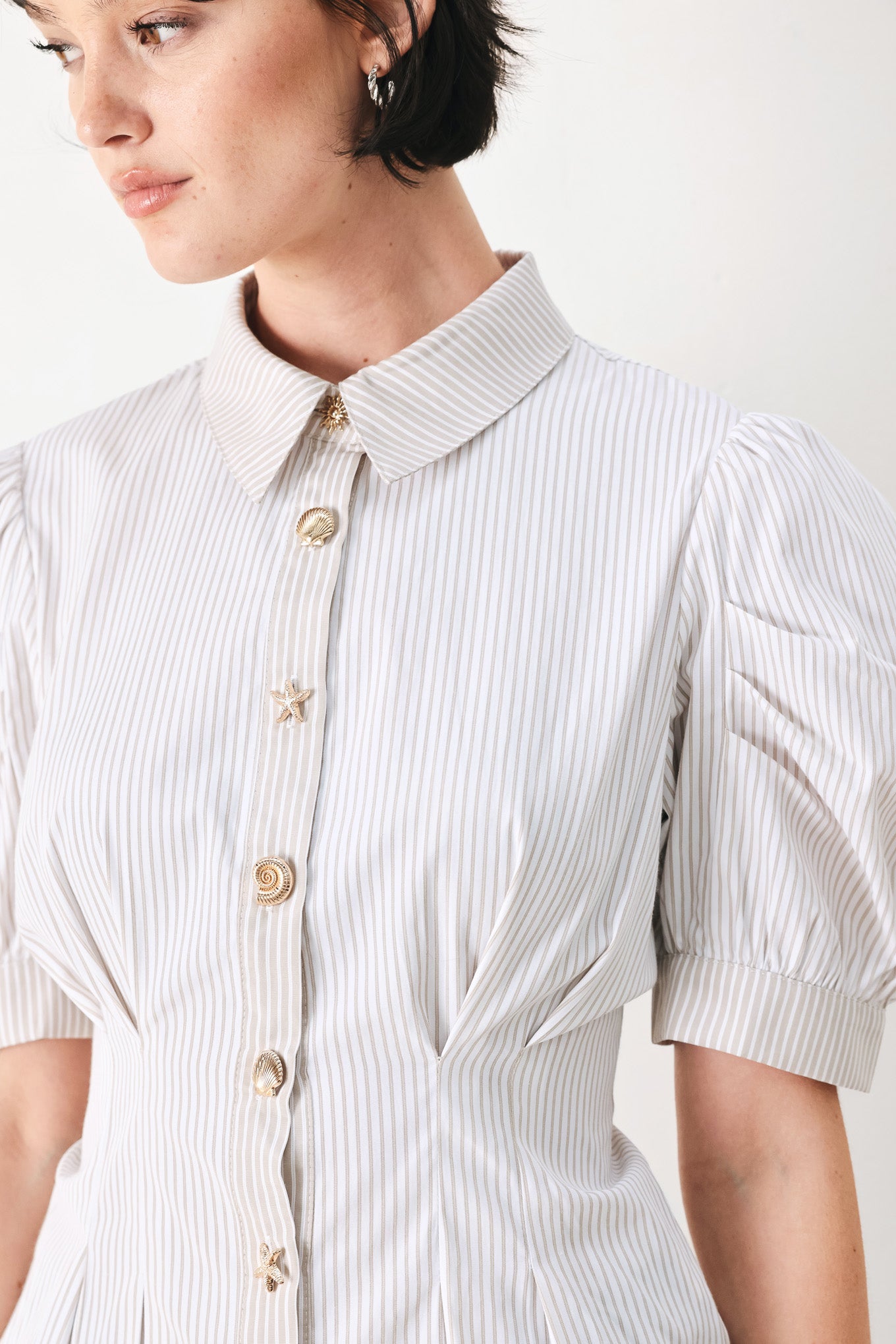 Woman wearing a taupe and white striped woven top featuring short puff sleeve, front button down, corset waist and peplum | FREEMARKET
