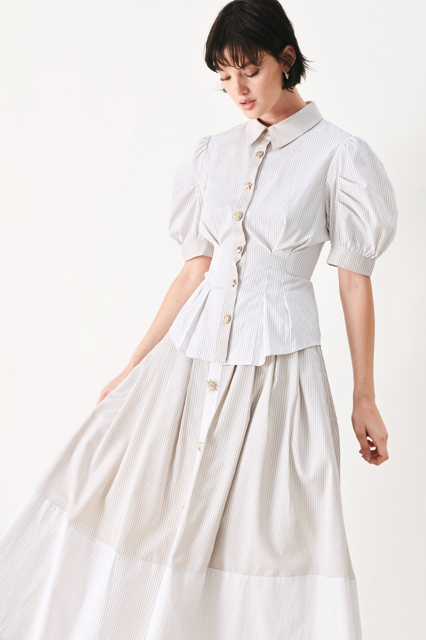 Woman wearing a taupe and white striped woven top featuring short puff sleeve, front button down, corset waist and peplum | FREEMARKET