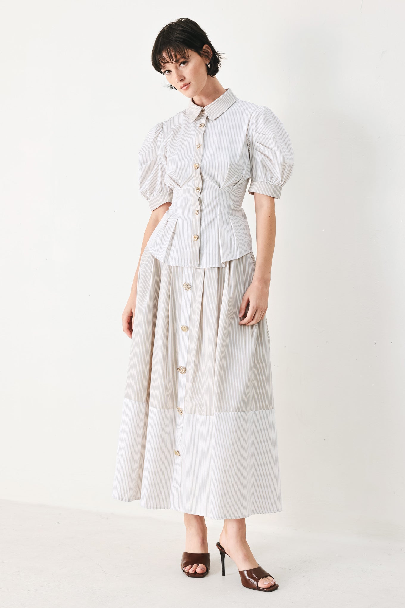 Woman wearing a taupe and white striped woven top featuring short puff sleeve, front button down, corset waist and peplum | FREEMARKET