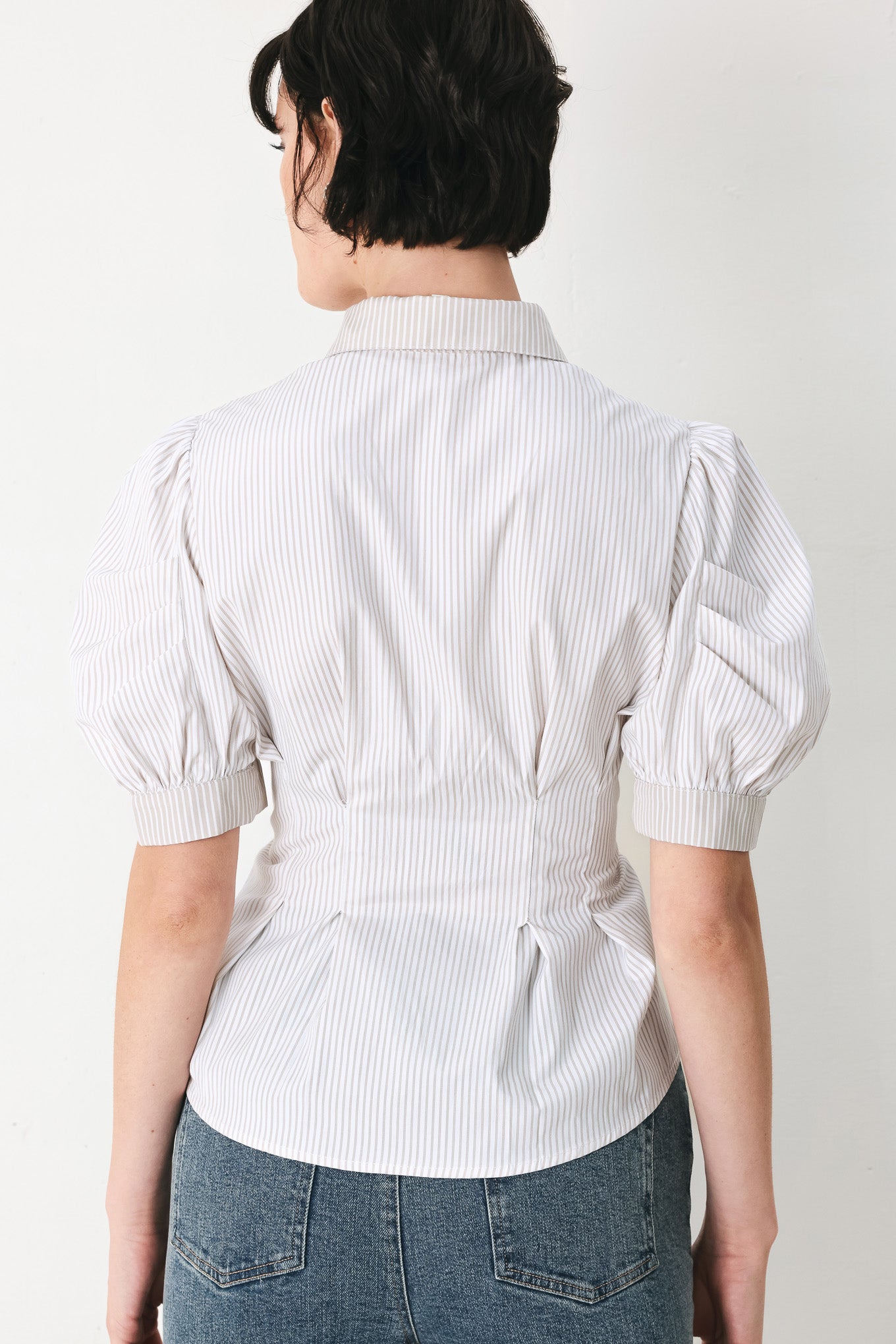 Woman wearing a taupe and white striped woven top featuring short puff sleeve, front button down, corset waist and peplum | FREEMARKET