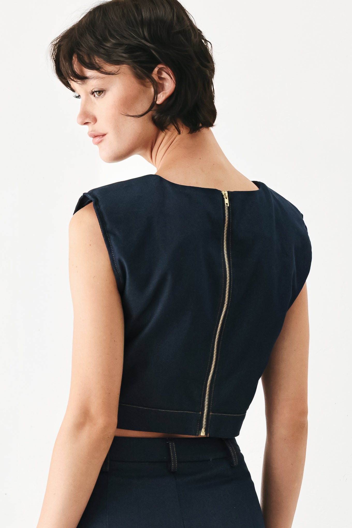 Woman wearing a navy blue sleeveless crop top with round neckline, hardware detail and back zipper closure | FREEMARKET