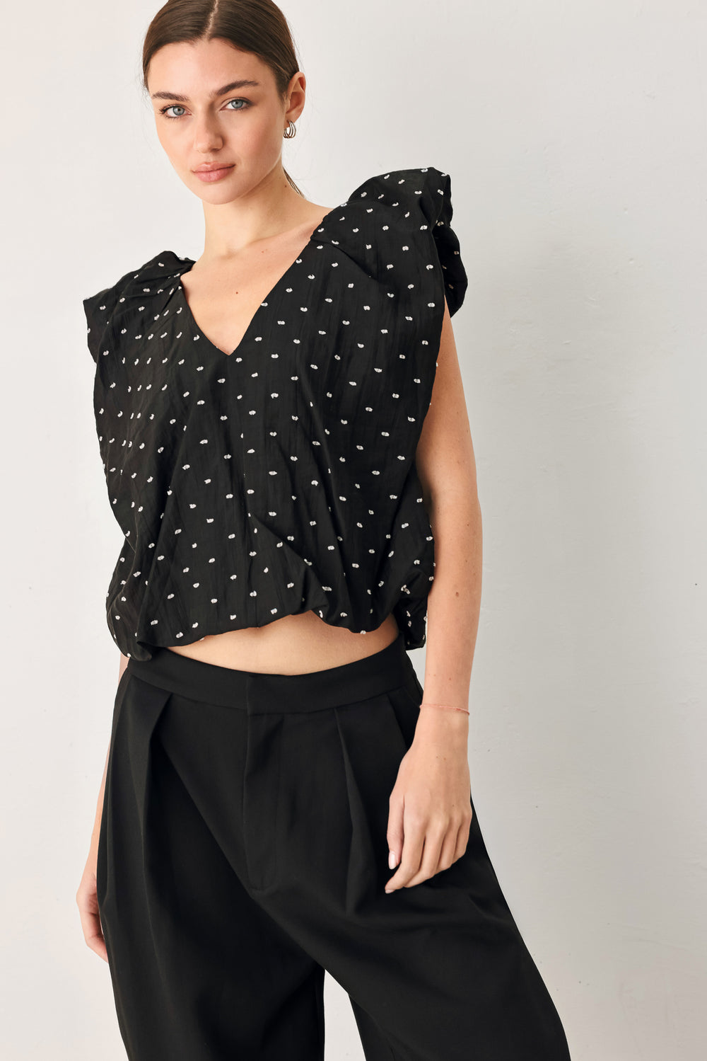 Woman wearing a black polka dot top featuring V neckline with bubble sleeve and waist | FREEMARKET