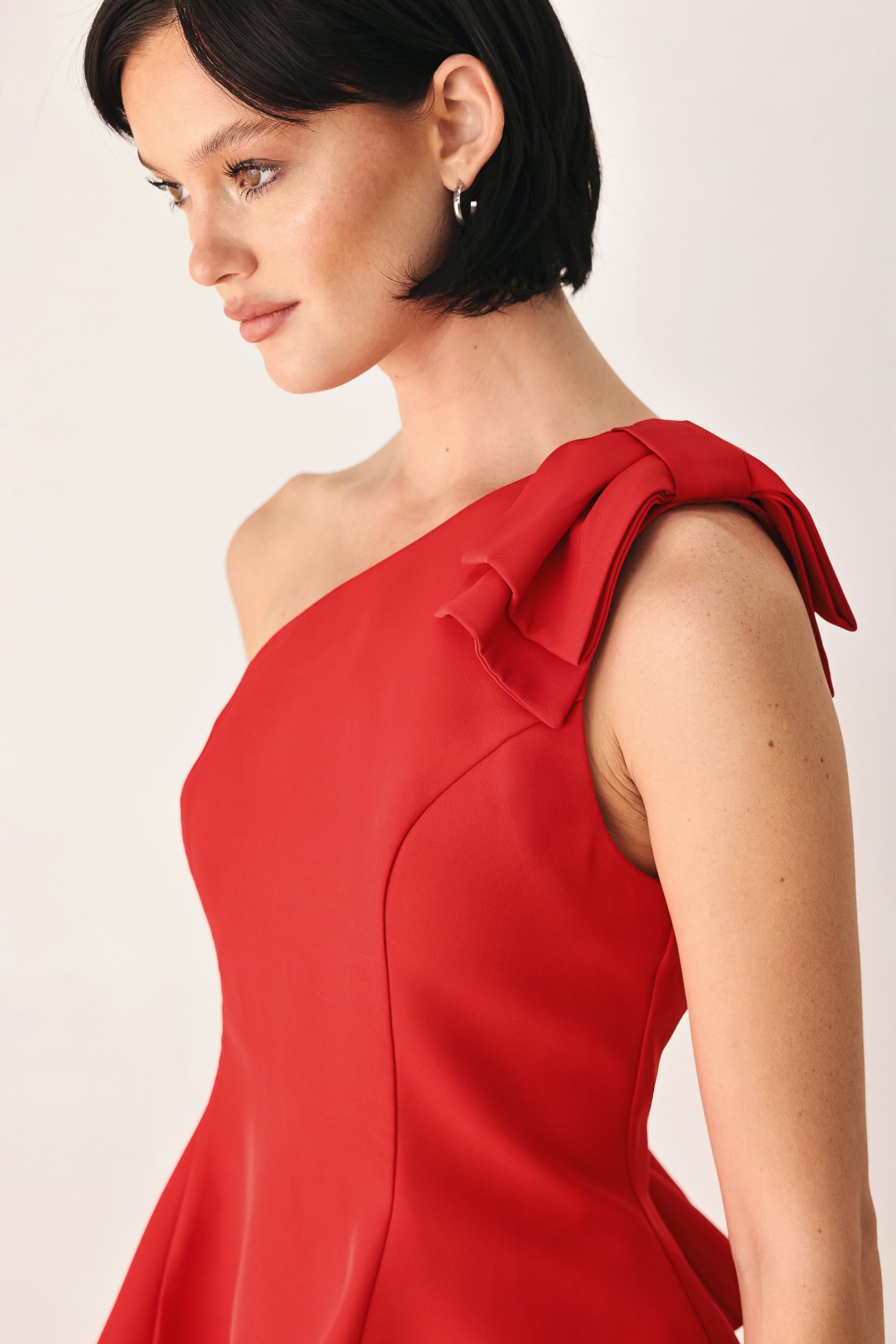 A woman modeling a bright red one-shoulder peplum top with a ruffled shoulder detail | FREEMARKET