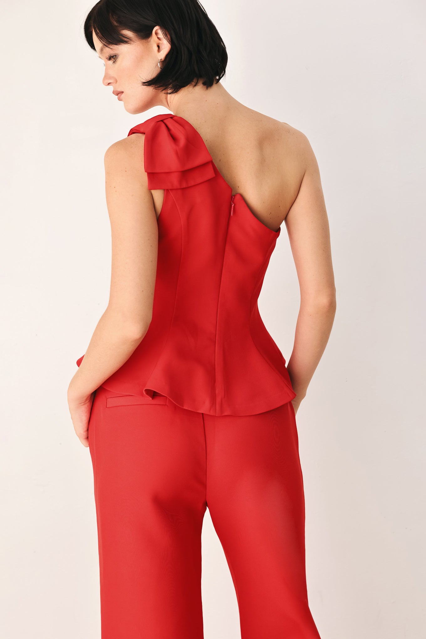 A woman modeling a bright red one-shoulder peplum top with a ruffled shoulder detail | FREEMARKET