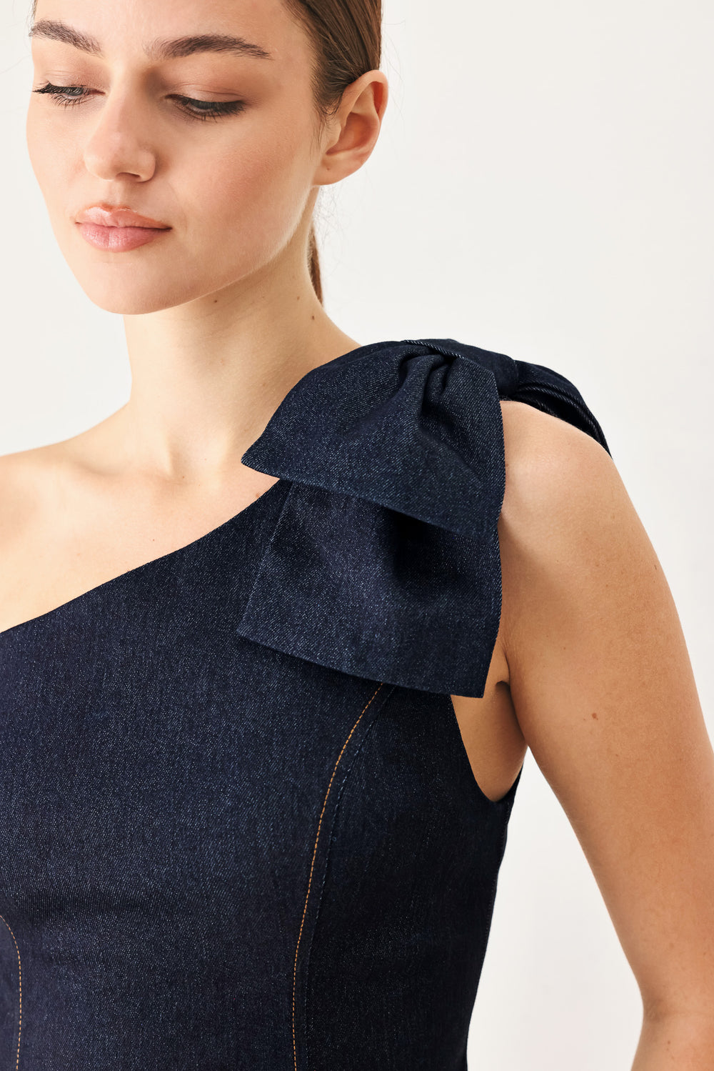 Woman wearing a dark blue denim one-shoulder peplum top with bow detail | Flying Tomato