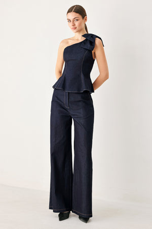 Woman wearing a dark blue denim one-shoulder peplum top with bow detail | Flying Tomato