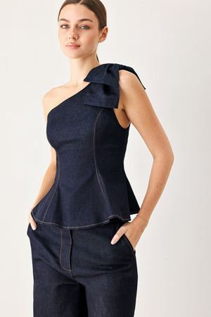 Woman wearing a dark blue denim one-shoulder peplum top with bow detail | Flying Tomato