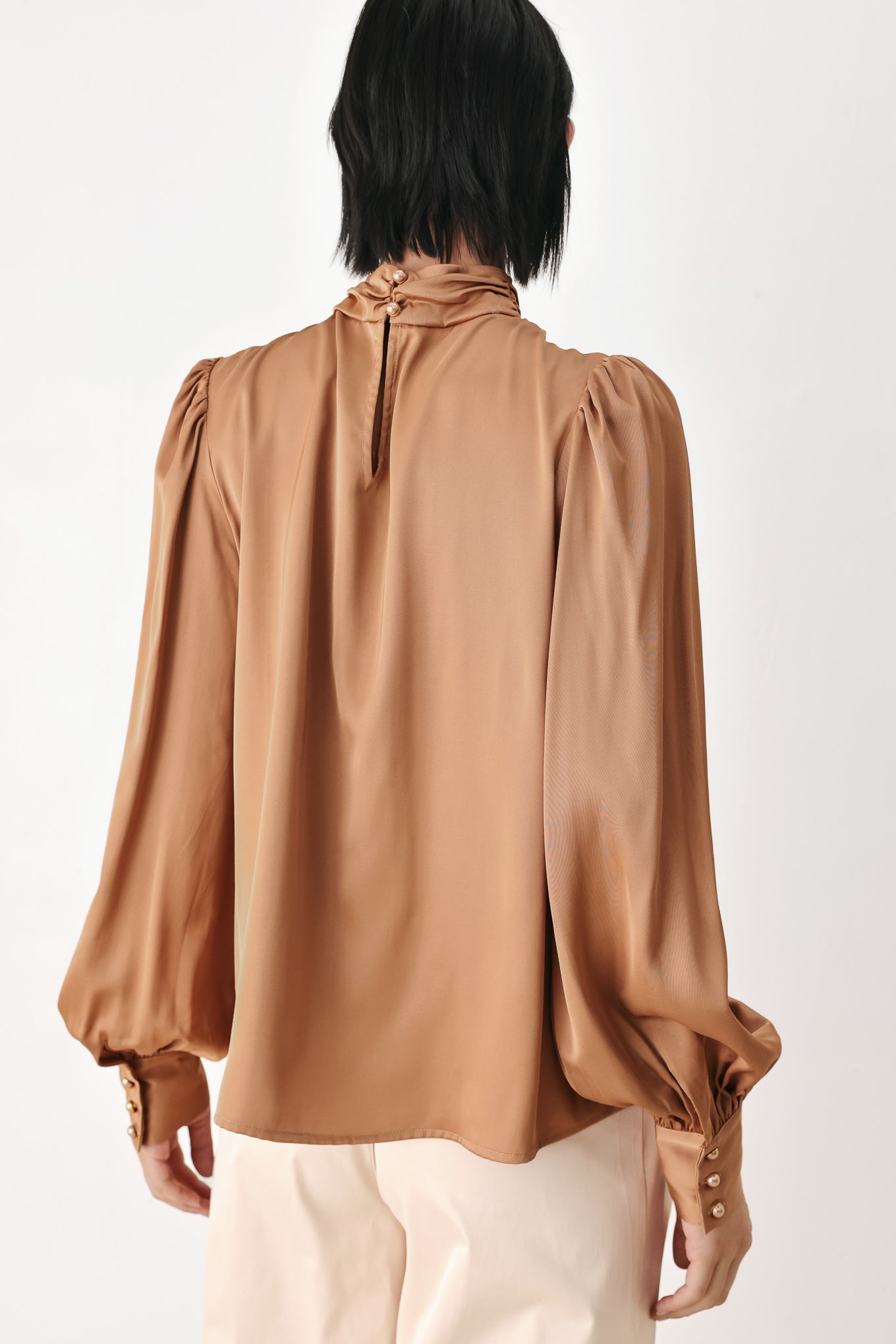 A woman wearing a bronze long-sleeve blouse with a gathered high neck and voluminous sleeves | FREEMARKET