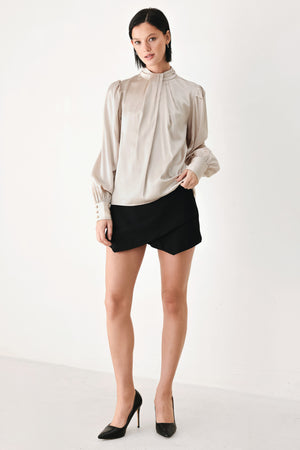 A woman wearing a champagne ivory long-sleeve blouse with a gathered high neck and voluminous sleeves | FREEMARKET