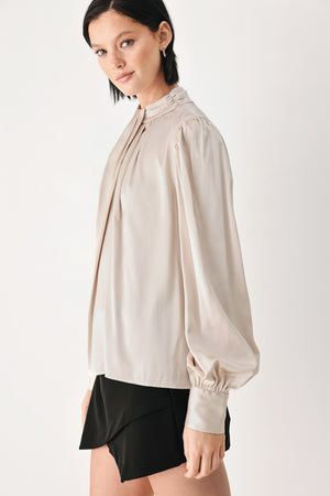 A woman wearing a champagne ivory long-sleeve blouse with a gathered high neck and voluminous sleeves | FREEMARKET
