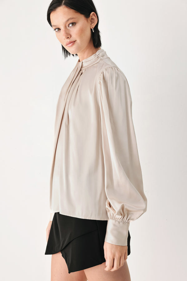 A woman wearing a champagne ivory long-sleeve blouse with a gathered high neck and voluminous sleeves | FREEMARKET