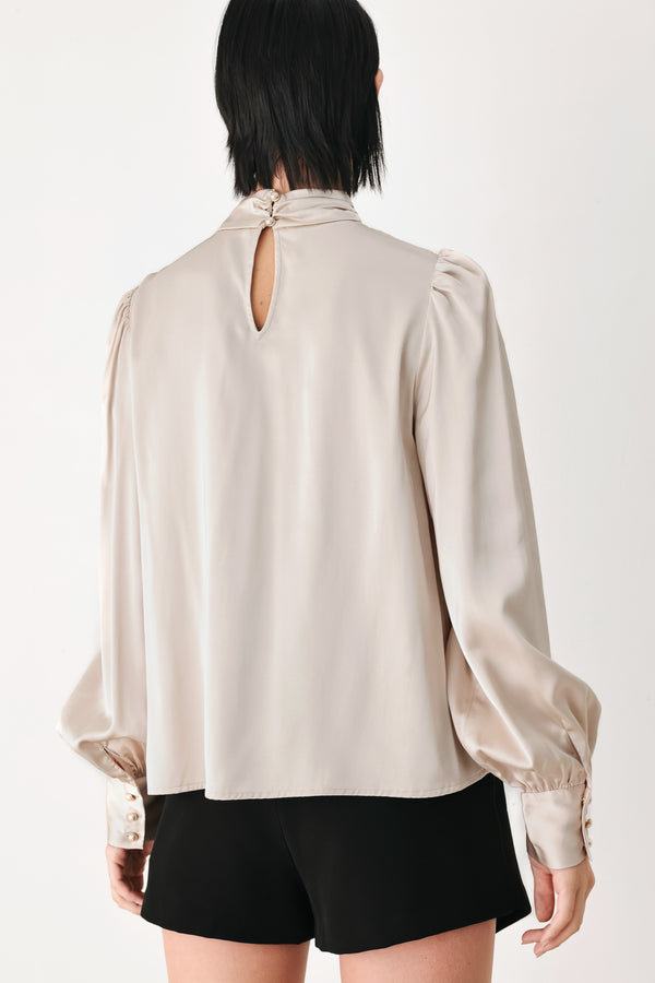 A woman wearing a champagne ivory long-sleeve blouse with a gathered high neck and voluminous sleeves | FREEMARKET