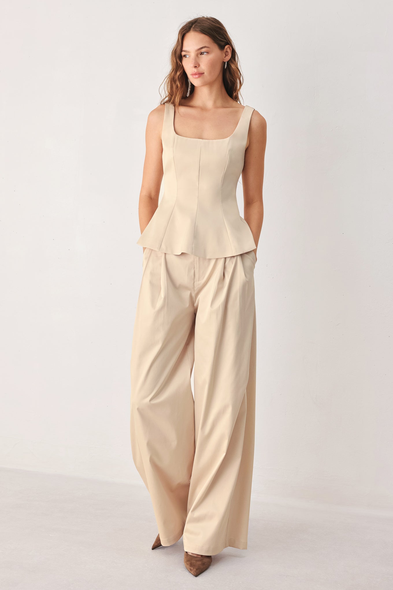 A woman modeling a champagne satin-like sleeveless top with a square neckline and structured peplum waist | FREEMARKET