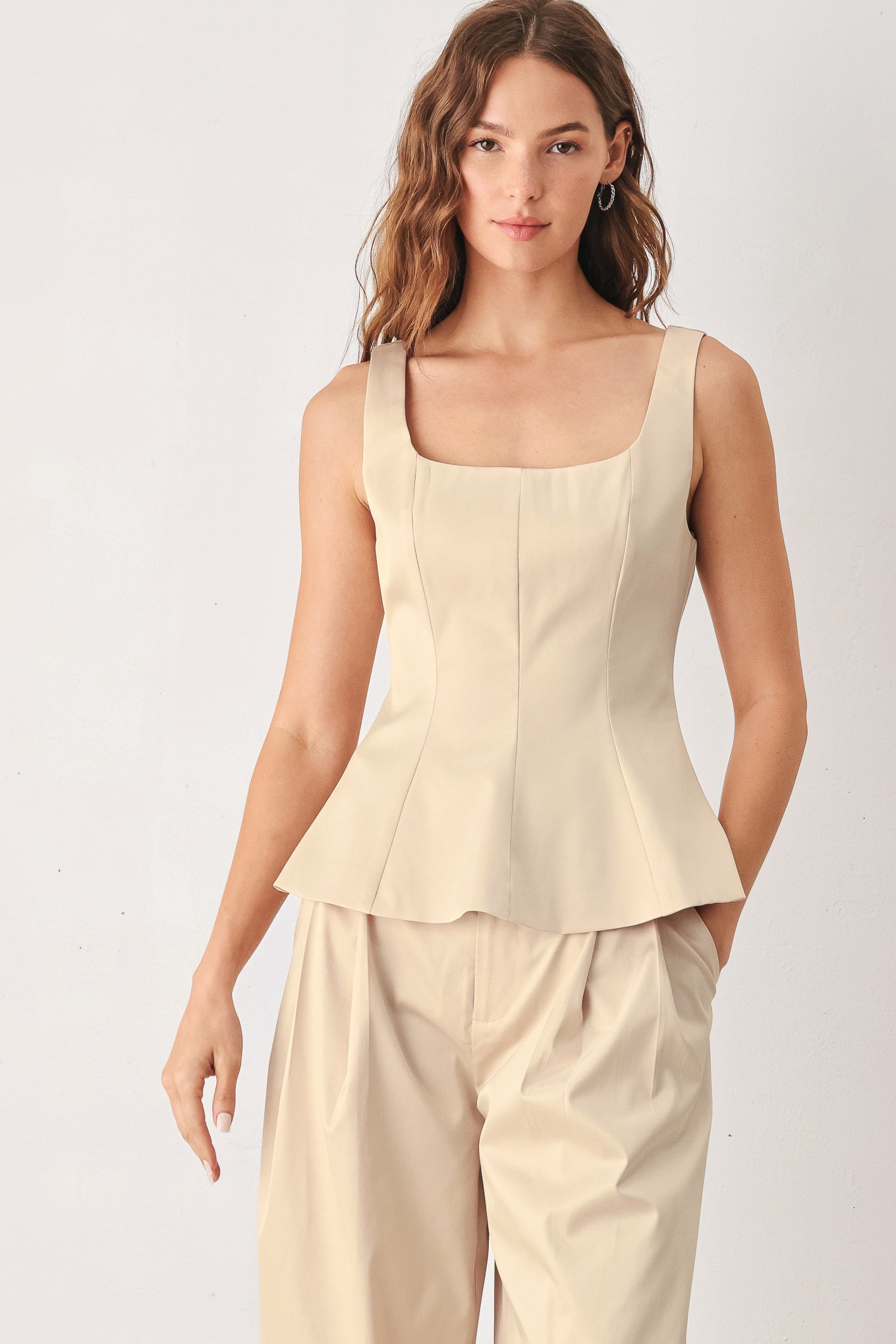 A woman modeling a champagne satin-like sleeveless top with a square neckline and structured peplum waist | FREEMARKET