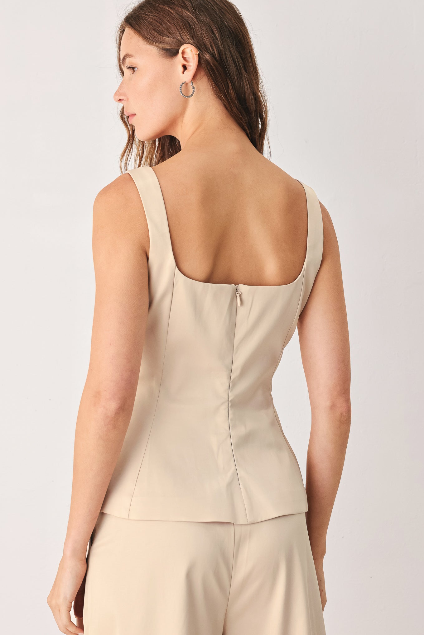 A woman modeling a champagne satin-like sleeveless top with a square neckline and structured peplum waist | FREEMARKET