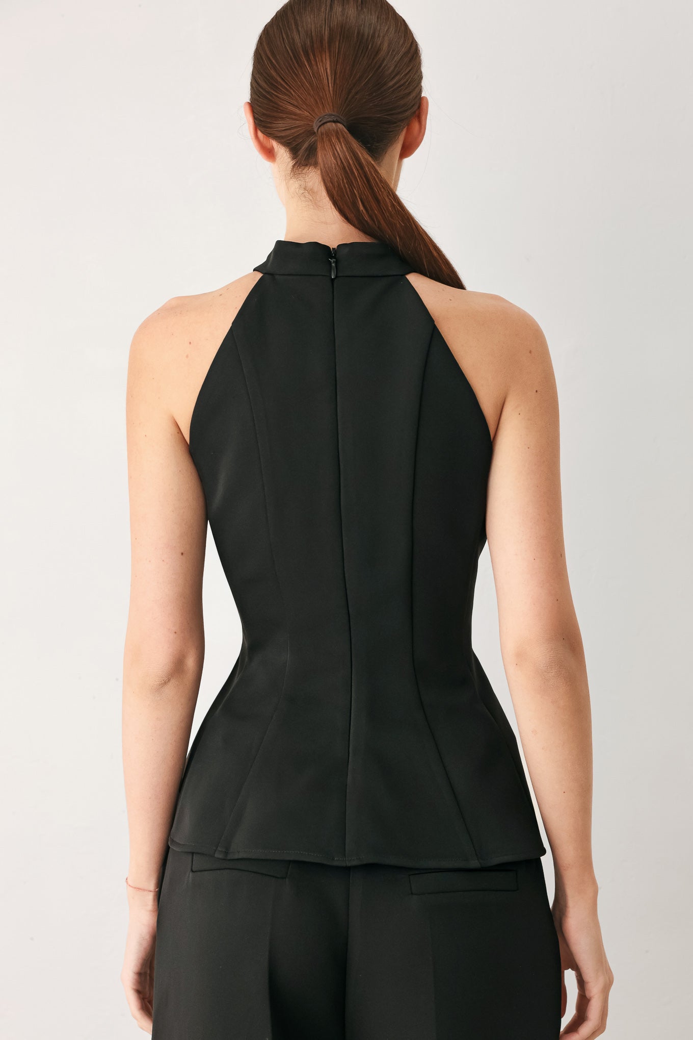 Woman wearing a black solid woven top with halter neckline, peplum and back zipper closure | FREEMARKET