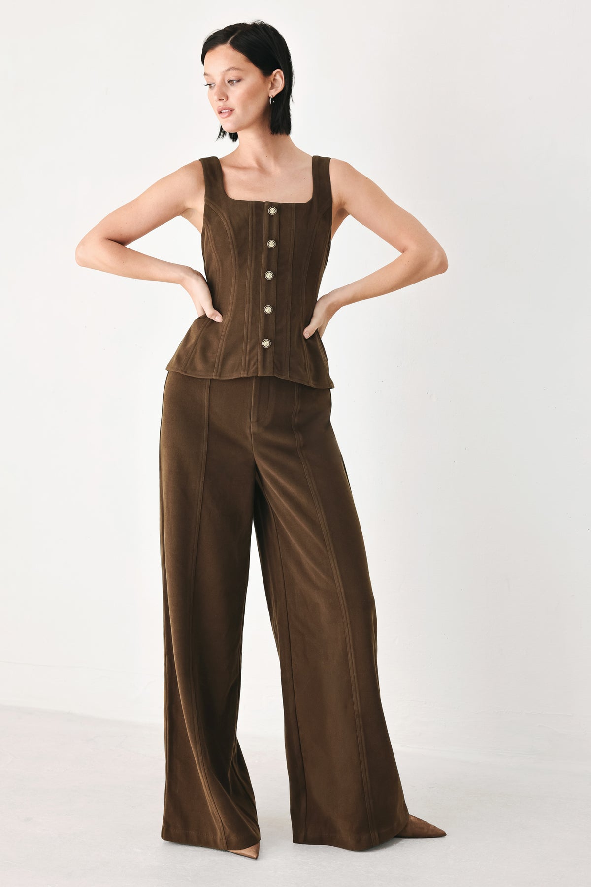 A woman wearing a brown sleeveless vest with a square neckline, front button closure, and vertical seam detailing | FREEMARKET