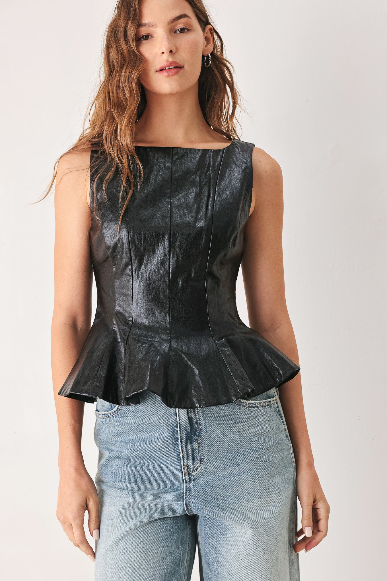 A woman wearing a sleeveless black faux-leather peplum top | FREEMARKET