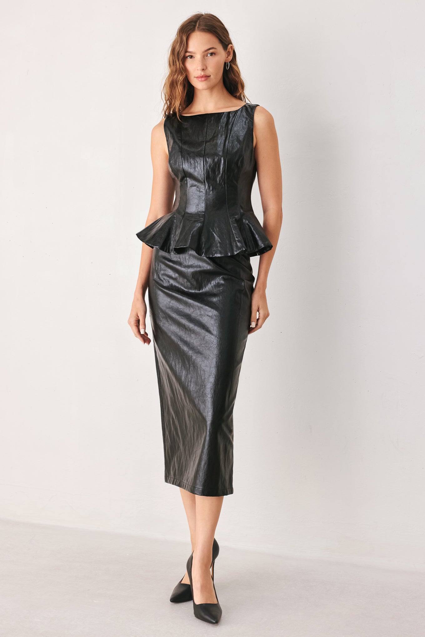 A woman wearing a sleeveless black faux-leather peplum top | FREEMARKET