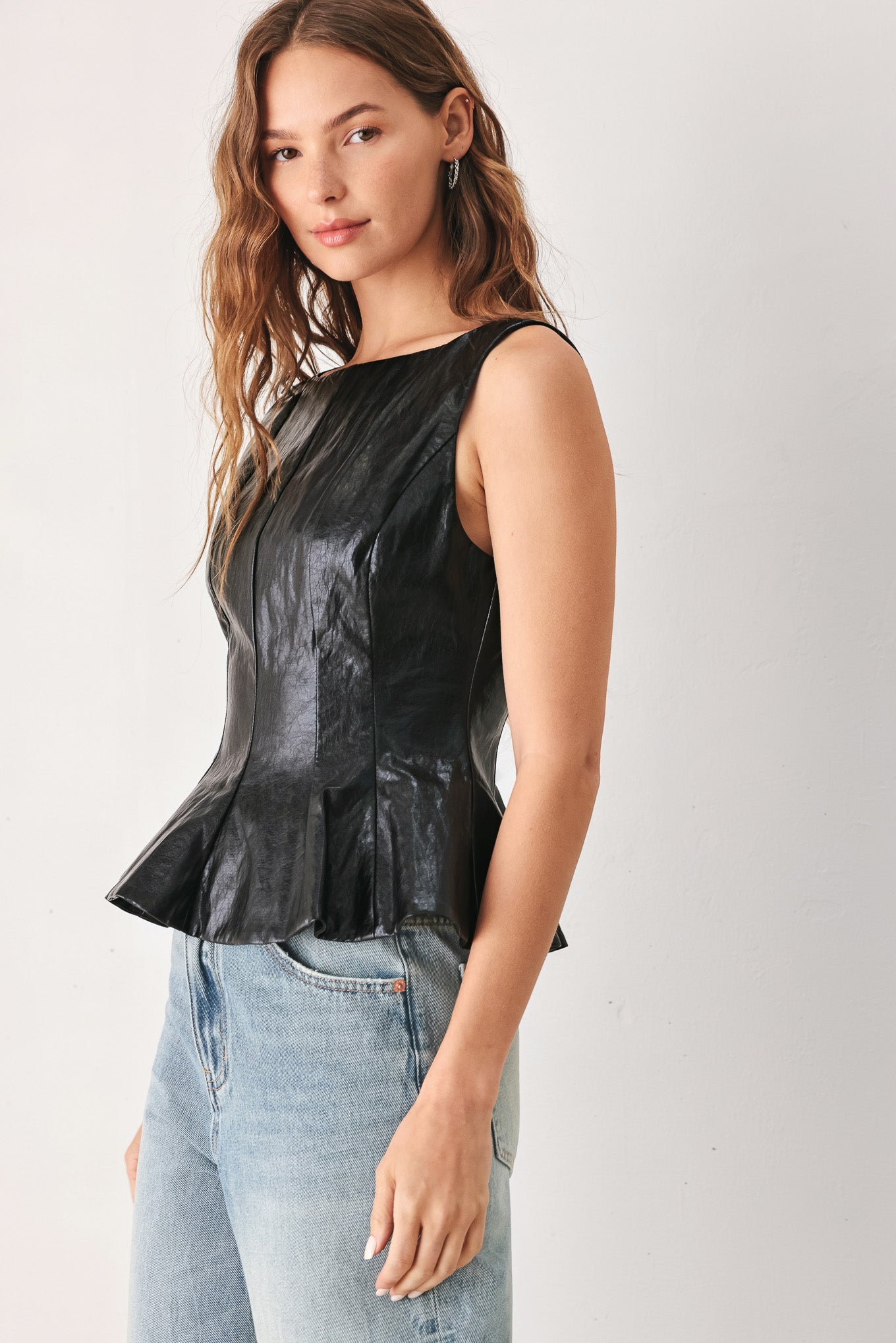 A woman wearing a sleeveless black faux-leather peplum top | FREEMARKET