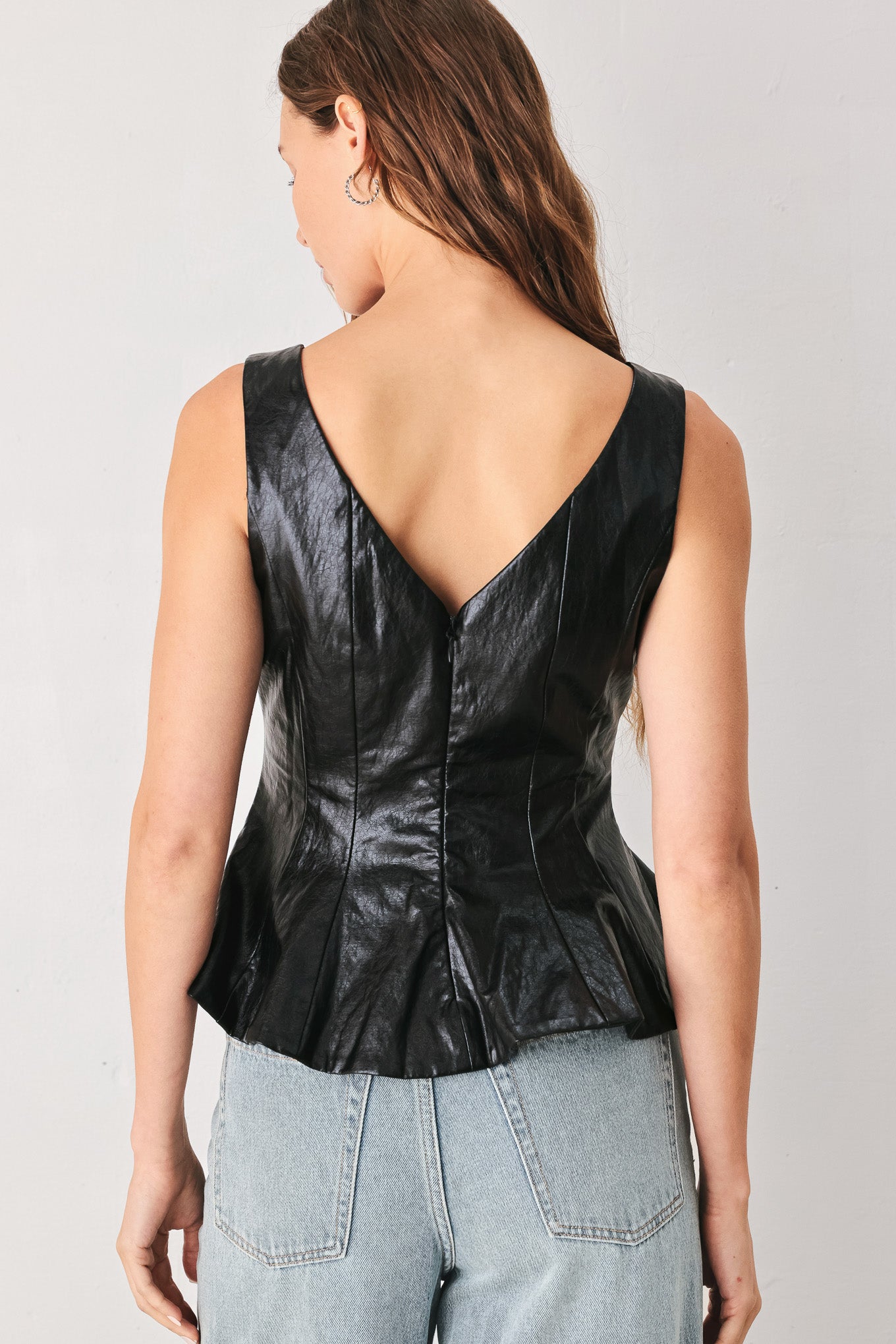A woman wearing a sleeveless black faux-leather peplum top | FREEMARKET