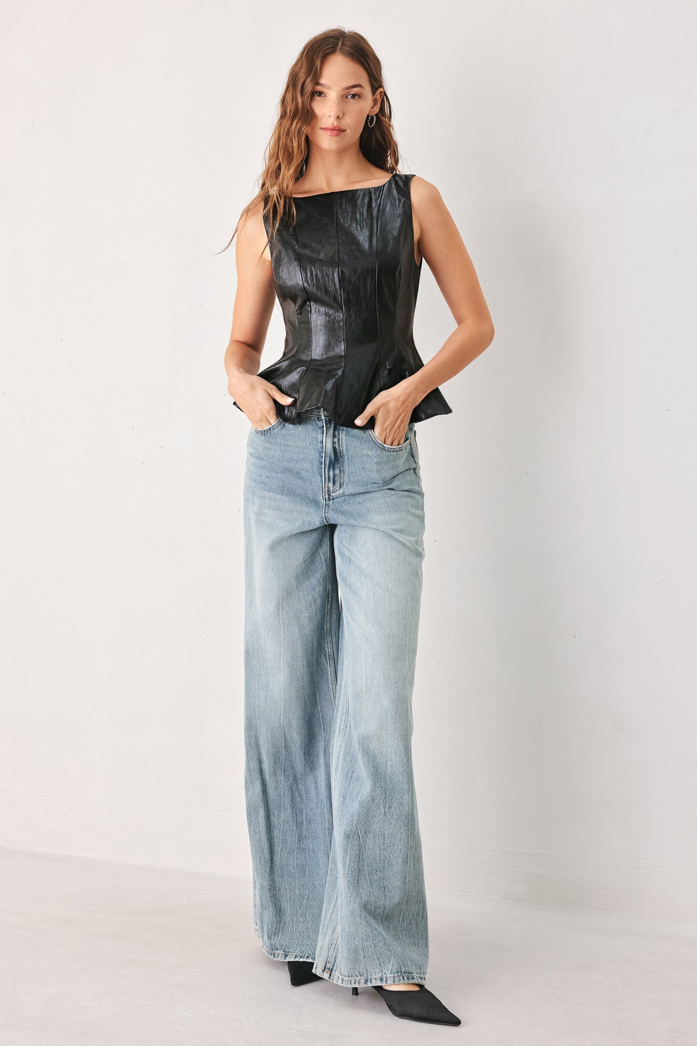 A woman wearing a sleeveless black faux-leather peplum top | FREEMARKET
