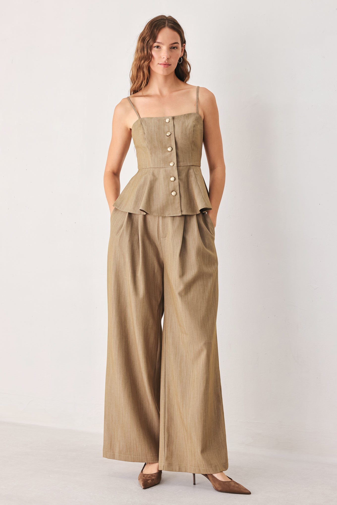 A woman wearing a tan linen camisole top with thin straps, a structured square neckline, peplum waist, and a front button closure | FREEMARKET